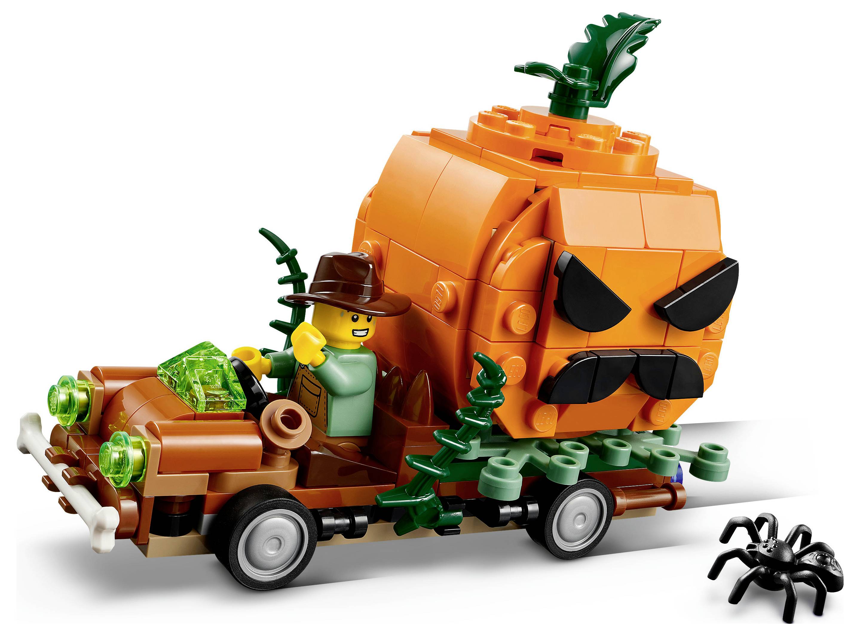 LEGO-ähnlicher orangefarbener Kürbis-Monstertruck mit einem Fahrer in einem braunen Hut, der einen kleinen Wagen mit grünen Kristallstücken zieht; eine schwarze Spinne sitzt in der Nähe.