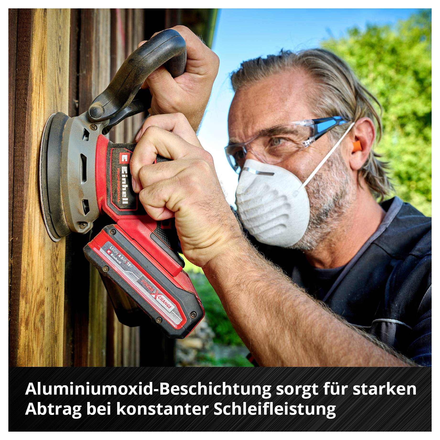 Mann mit Schutzmaske schleift Holz mit Exzenterschleifer; Hinweis: 'Aluminiumoxid-Beschichtung sorgt für starken Abtrag bei konstanter Schleifleistung'