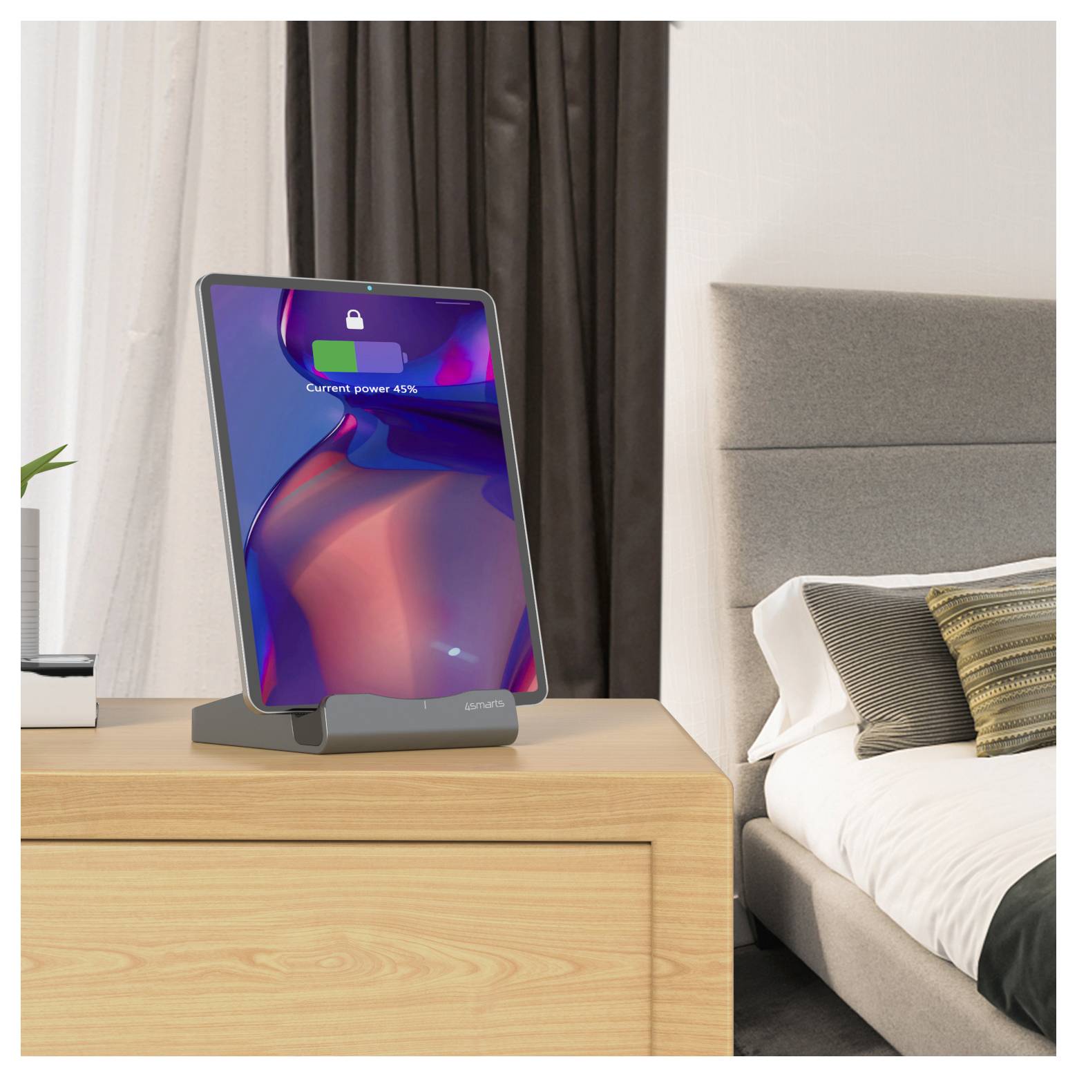 Tablet in einem Ständer auf einer Schlafzimmerkommode, auf dessen Bildschirm ein Batteriesymbol und „Aktuelle Leistung 45 %