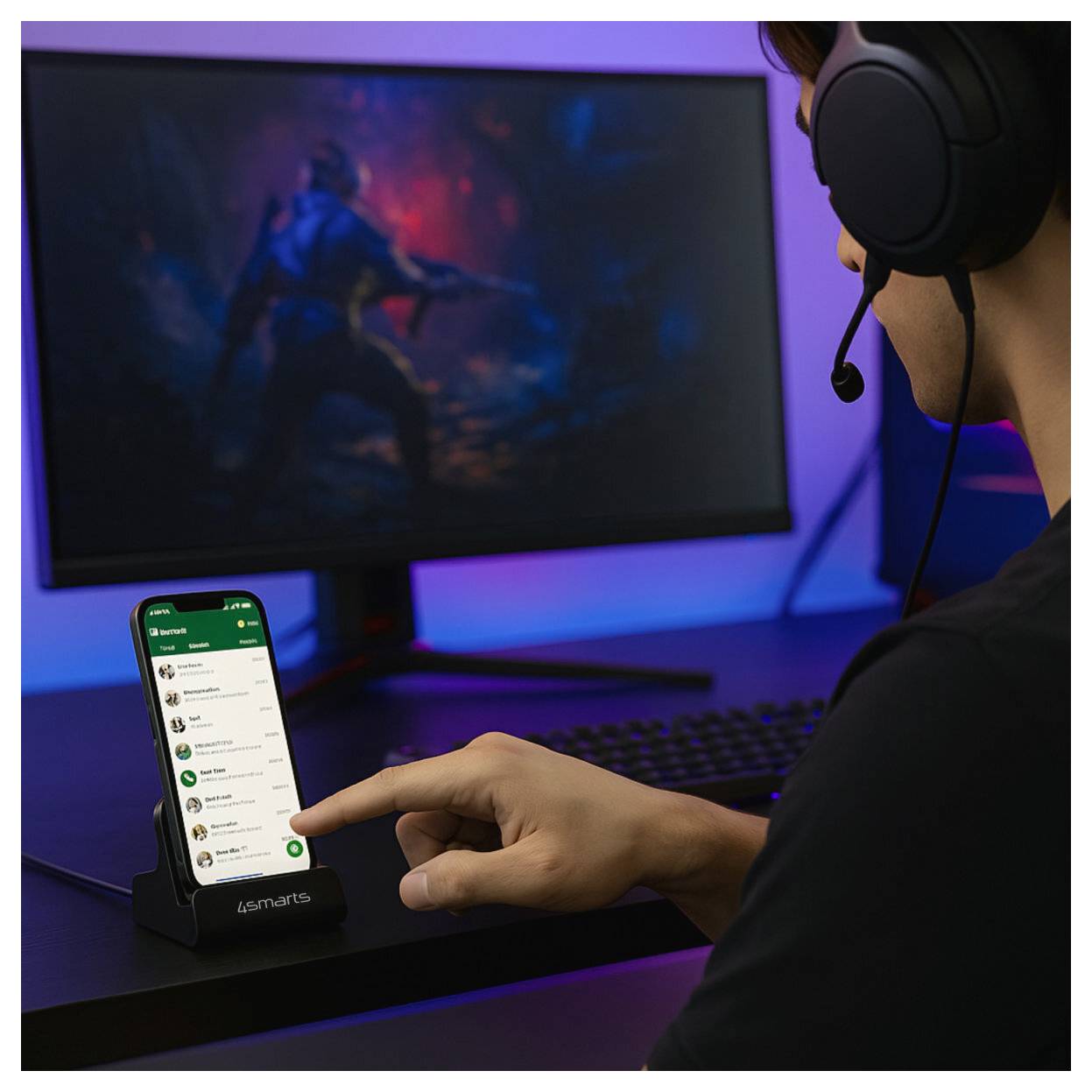 Eine Person mit Headset deutet auf ein Smartphone in einer Tischhalterung neben einem Gaming-Monitor und deutet auf Gaming- oder App-Nutzung hin.