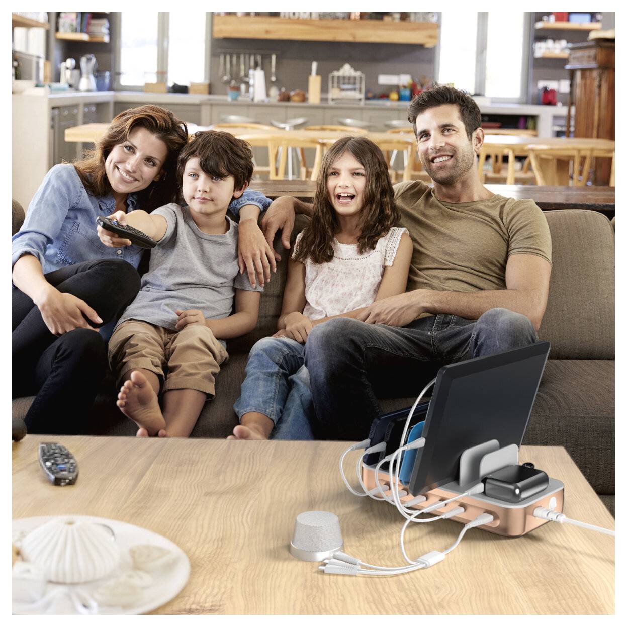 Eine vierköpfige Familie sitzt zusammen auf einem Sofa und schaut gemeinsam fern, mit einem Streaming-Gerät und Kabeln auf dem Couchtisch.