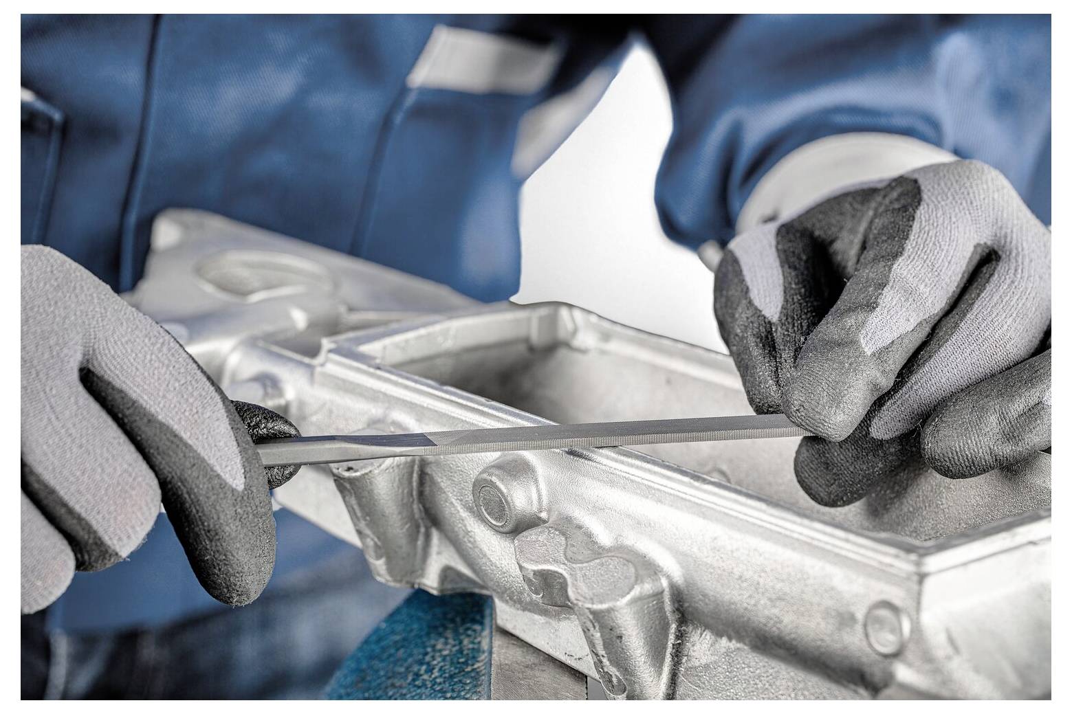 Mechaniker mit Handschuhen, der mit einem Metallwerkzeug einen silbernen Motor oder eine Maschinenkomponente inspiziert oder aufbricht.