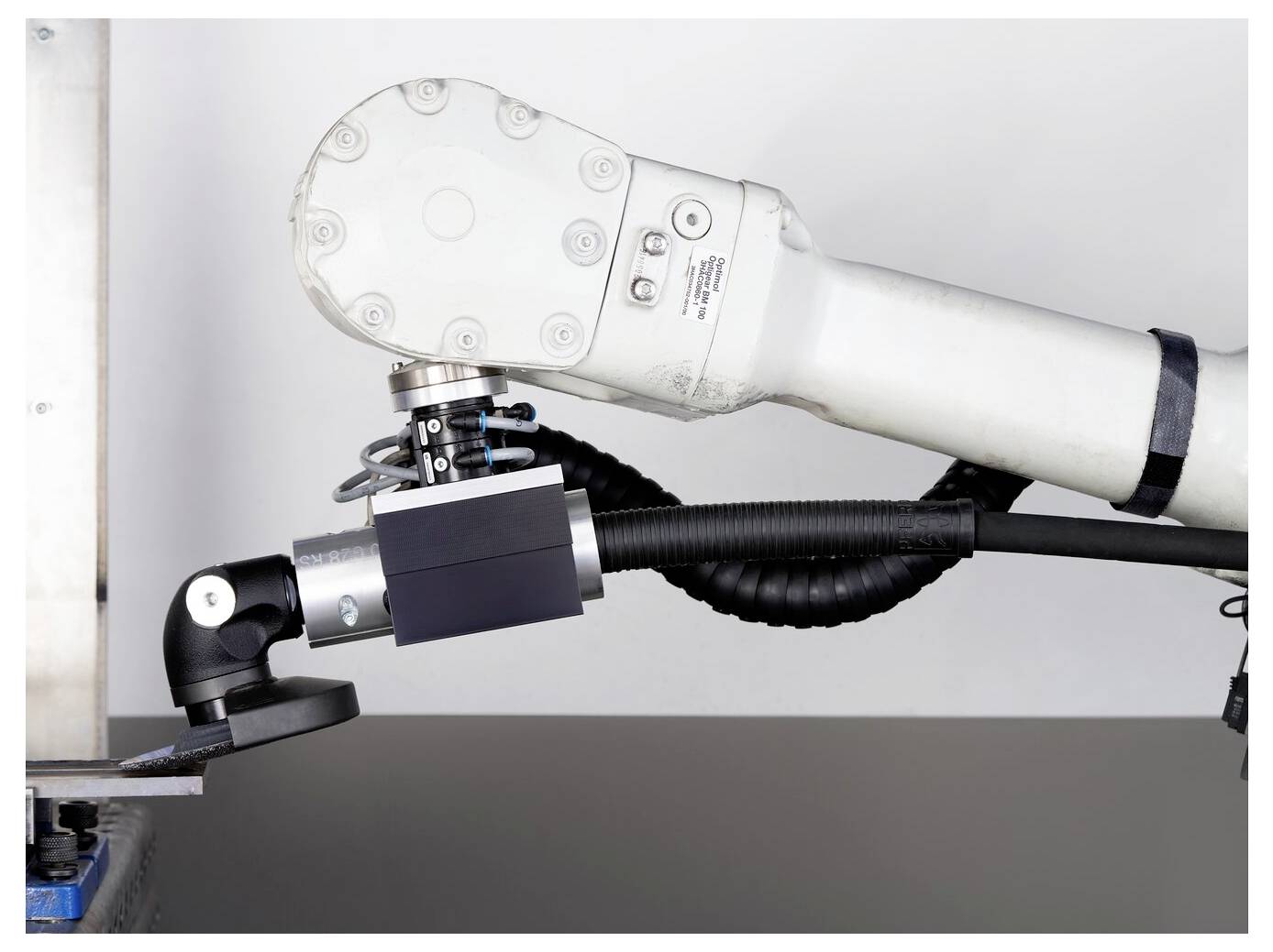 Industrial robotic arm with a grinding or cutting tool attached, positioned over a work surface, suggesting automated manufacturing or machining.
