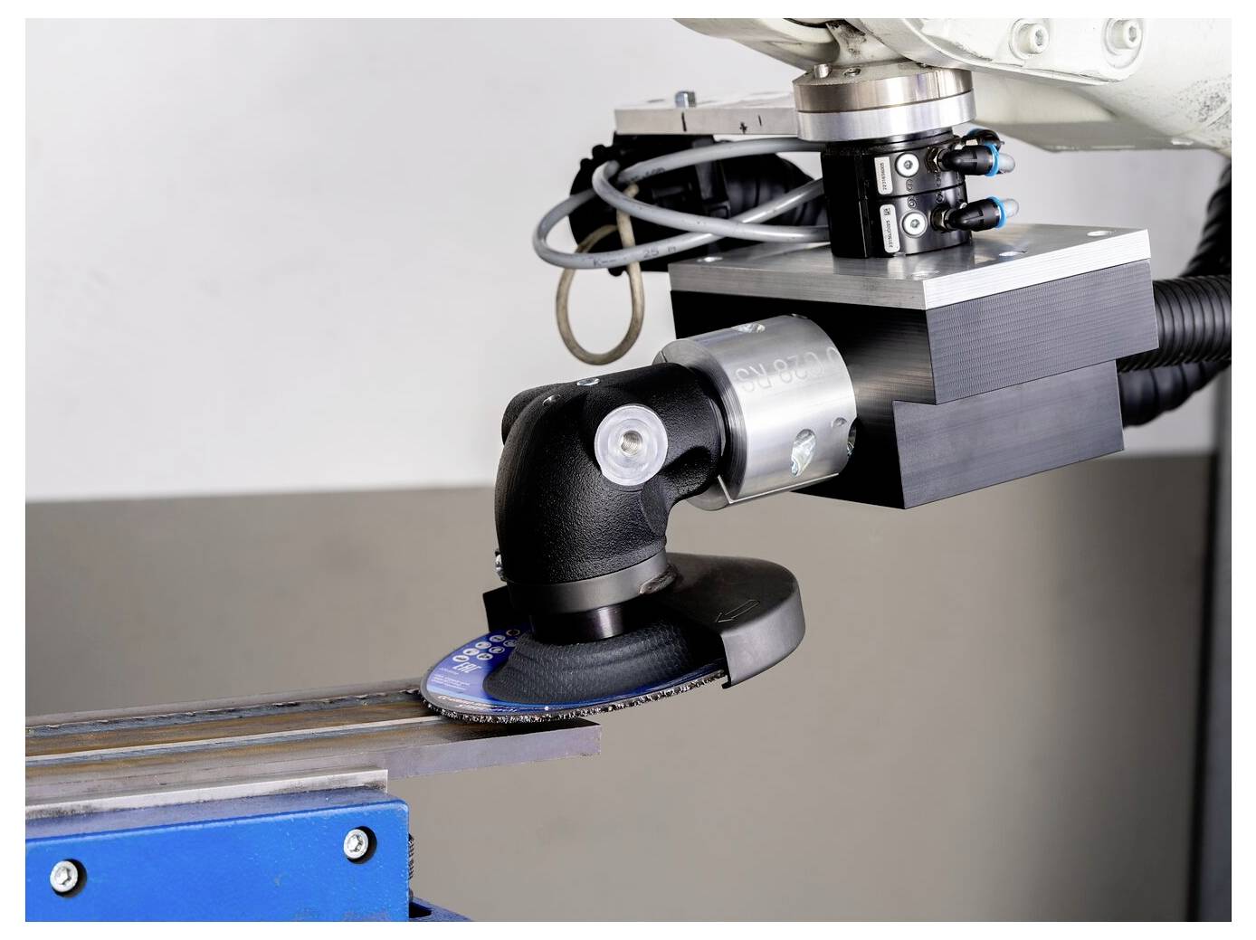 Robotic arm using a grinding/sanding tool on a metal workpiece in an industrial setting.
