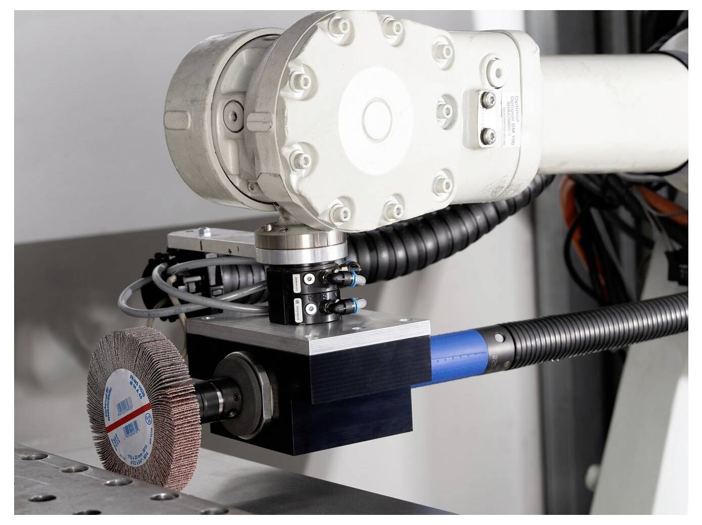 Industrieller Roboterarm mit montiertem Schleifrad, das ein Metallwerkstück auf einem Maschinentisch schleifen oder polieren.