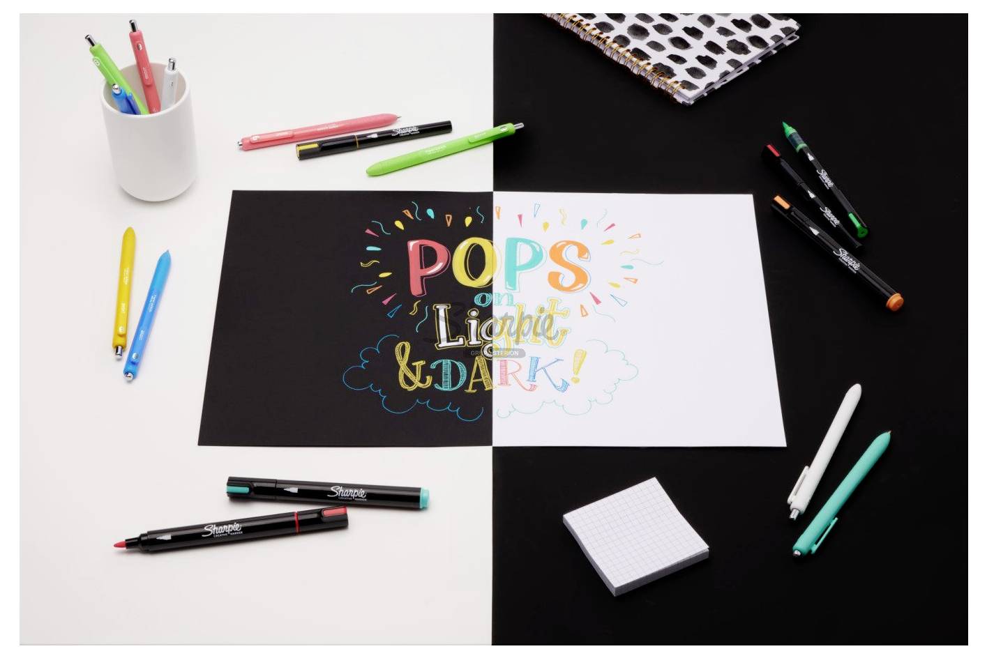Draufsicht auf ein Schriftdesign auf geteiltem schwarz-weißem Papier mit der Aufschrift „POPS on LIGHTER & DARK