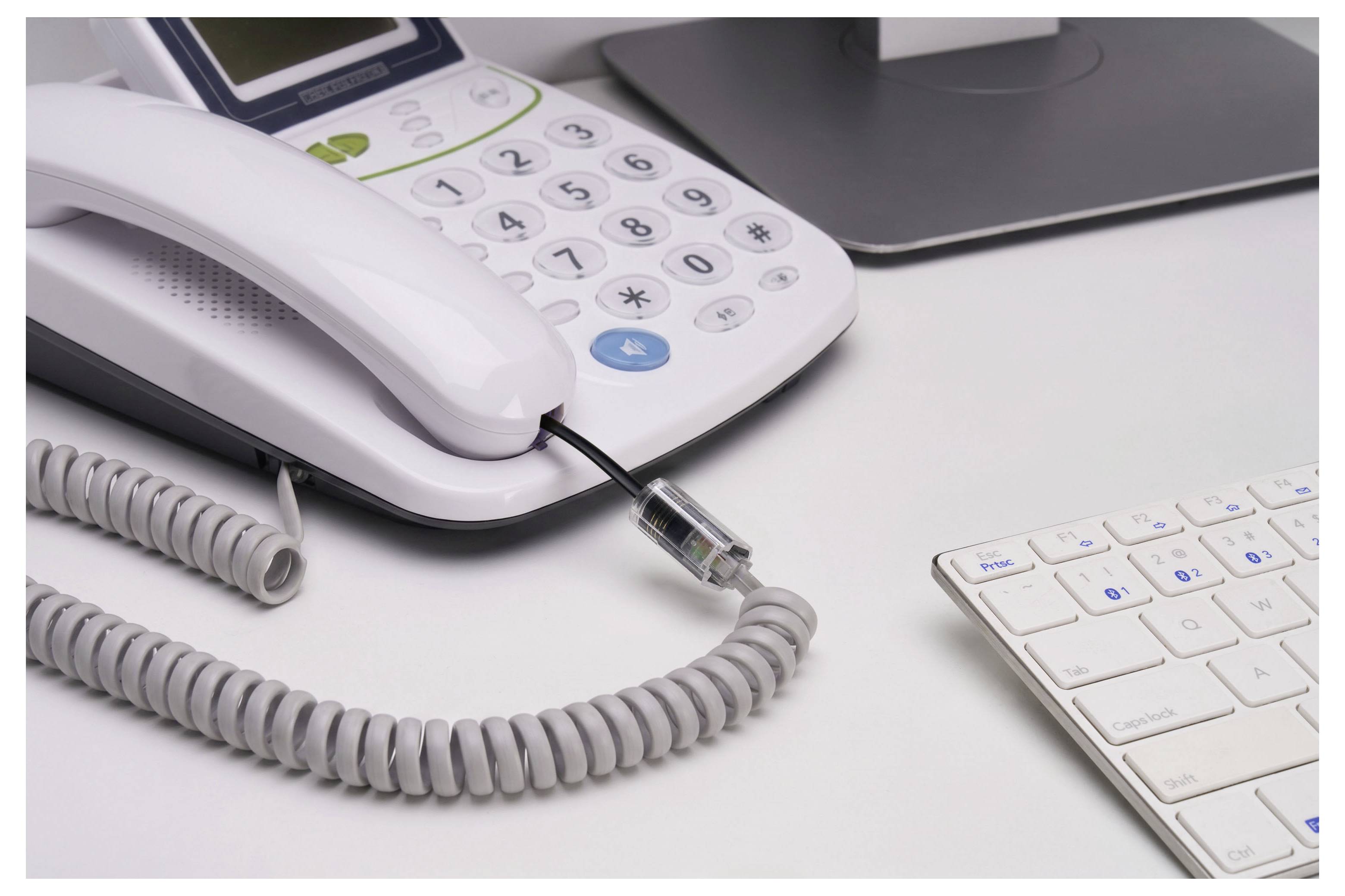 Weißer Büroschreibtisch mit einem Schnurtelefon, Spiralkabel, Ethernet-Kabel, Laptop und Tastatur, was auf einen verkabelten Büroarbeitsplatz hindeutet.
