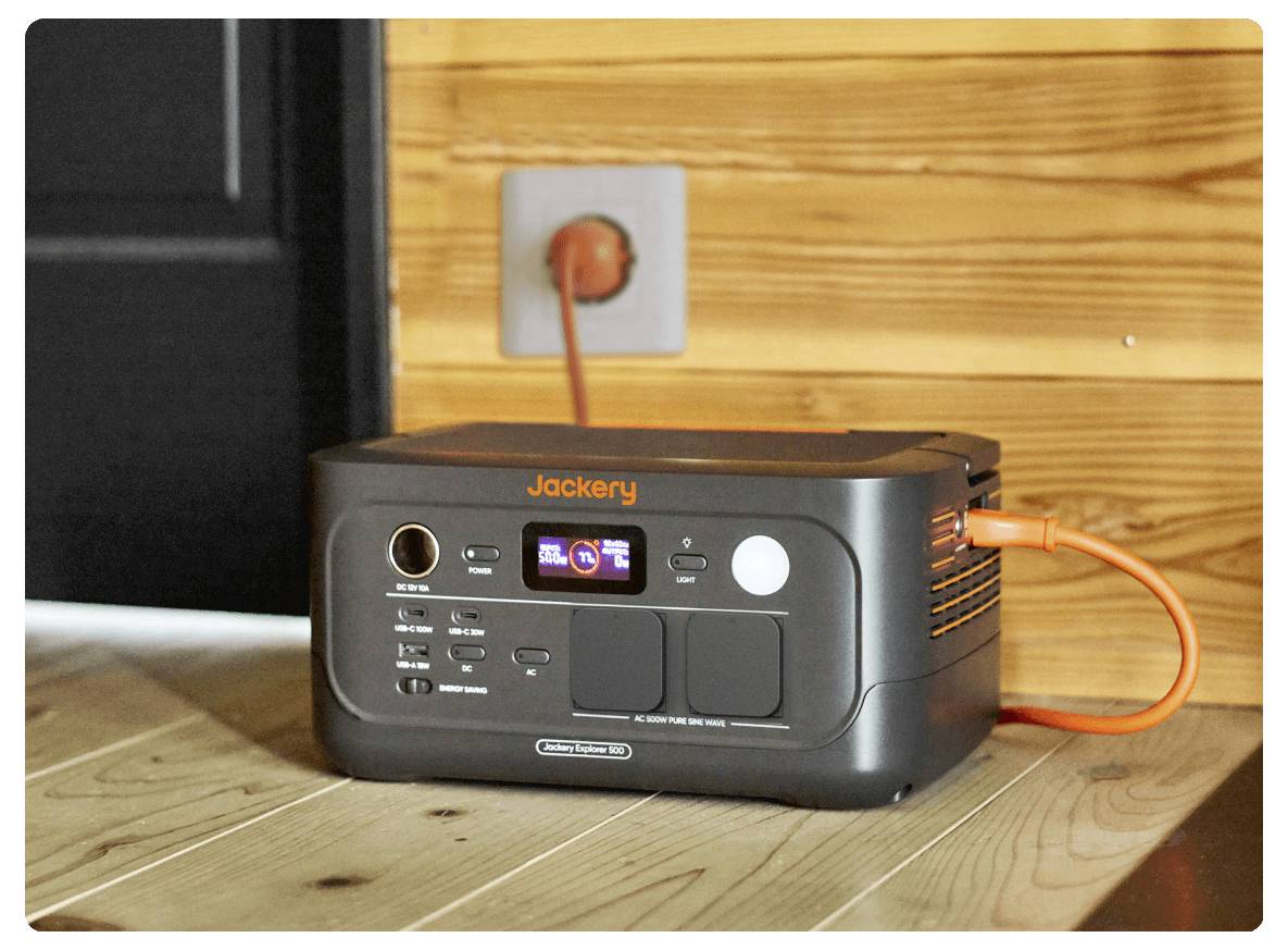 Jackery tragbare Stromstation, die in eine Wandsteckdose eingestöpselt ist und auf einem Holzboden vor einer holzvertäfelten Wand steht.