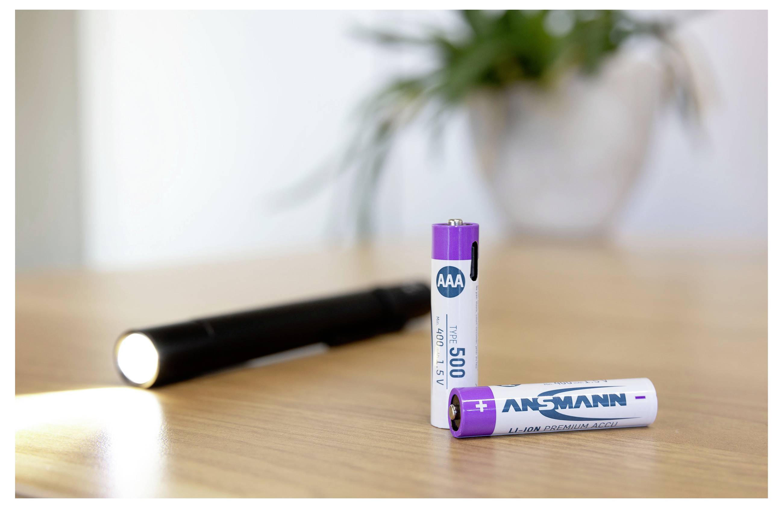 Drei AAA-Batterien auf einem Holztisch, mit einer schwarzen Taschenlampe dahinter und einer Batterie, die aufrecht davor steht.