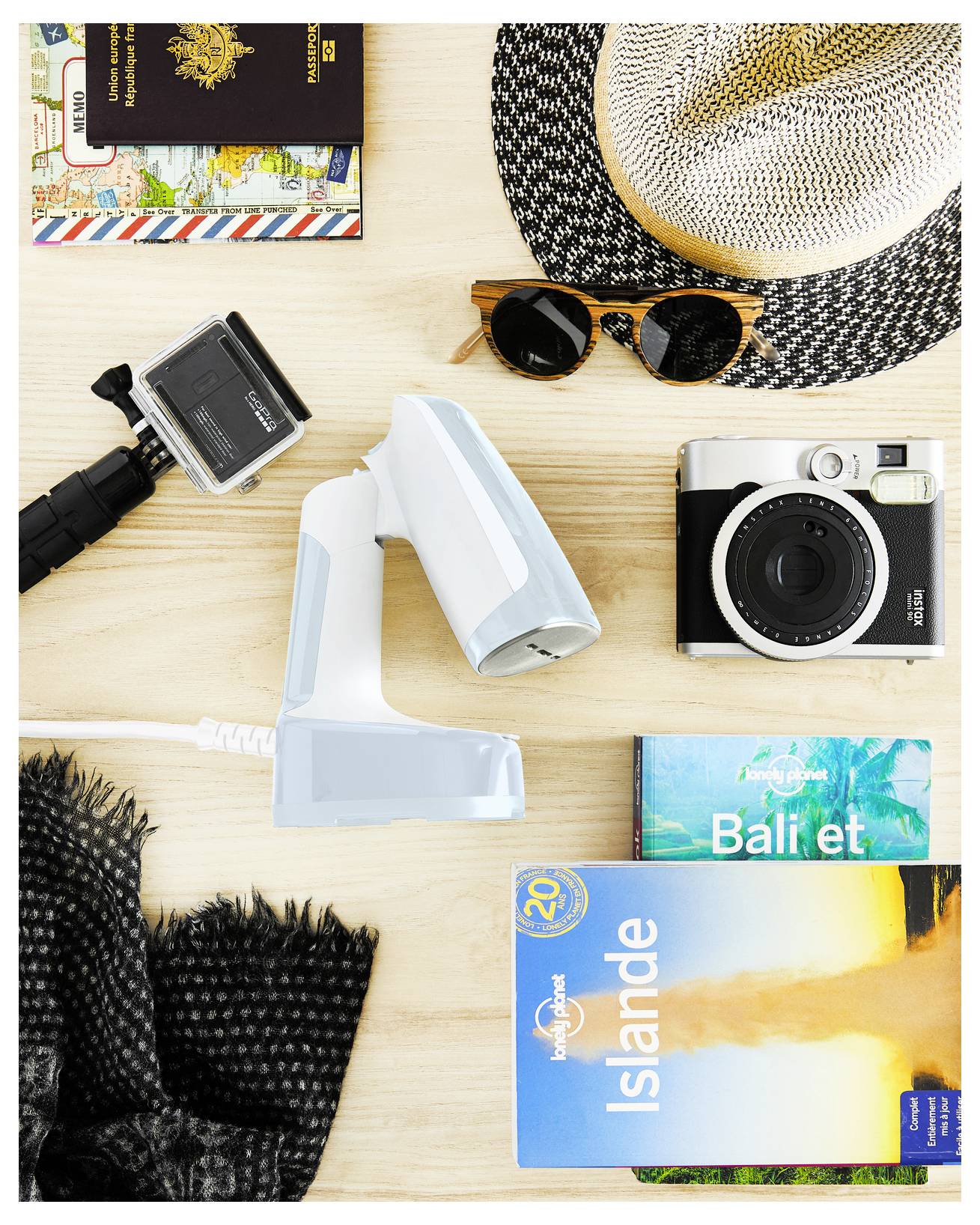 Flache Reiseanordnung mit einer Kamera, GoPro, Pass, Sonnenbrille, Sonnenhut und Reiseführern für Bali und Island auf einer Holzoberfläche.