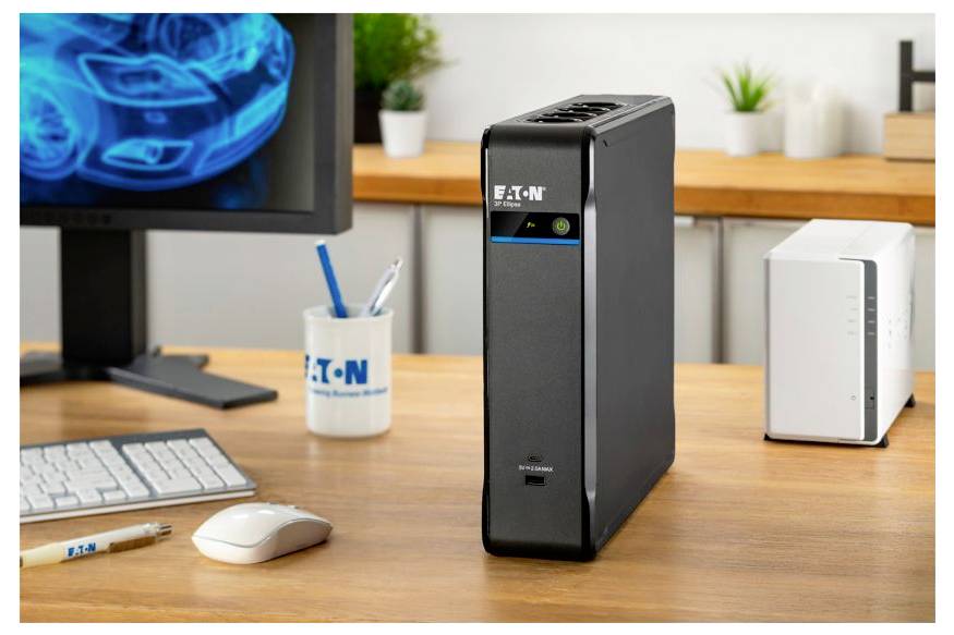 Eaton-Tisch-USV-Stromausfallschutzgerät, das auf einem Schreibtisch neben einem Computermonitor, einer Tastatur, einer Maus und Bürozubehör steht.