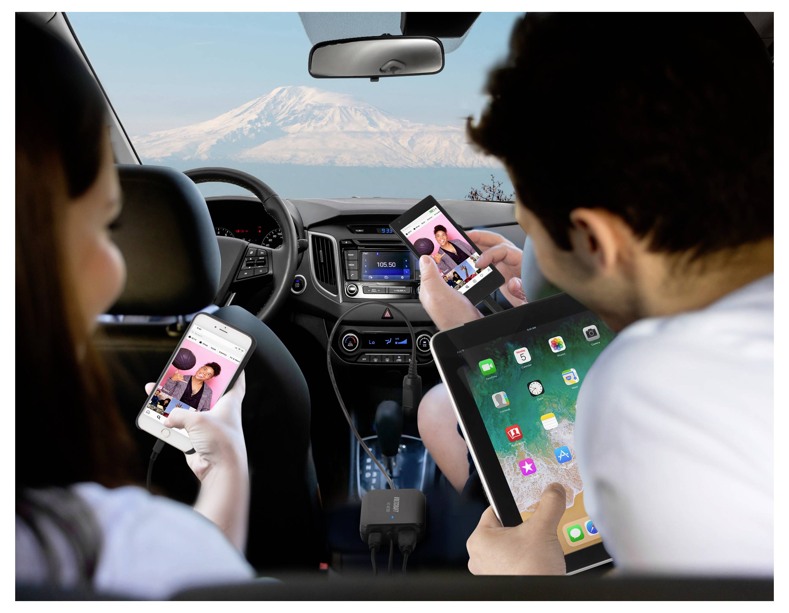 Zwei Fahrgäste nutzen ein Telefon und ein Tablet in einem Auto während der Fahrt, wobei ein Berg durch die Windschutzscheibe sichtbar ist, was auf abgelenktes Fahren hindeutet.