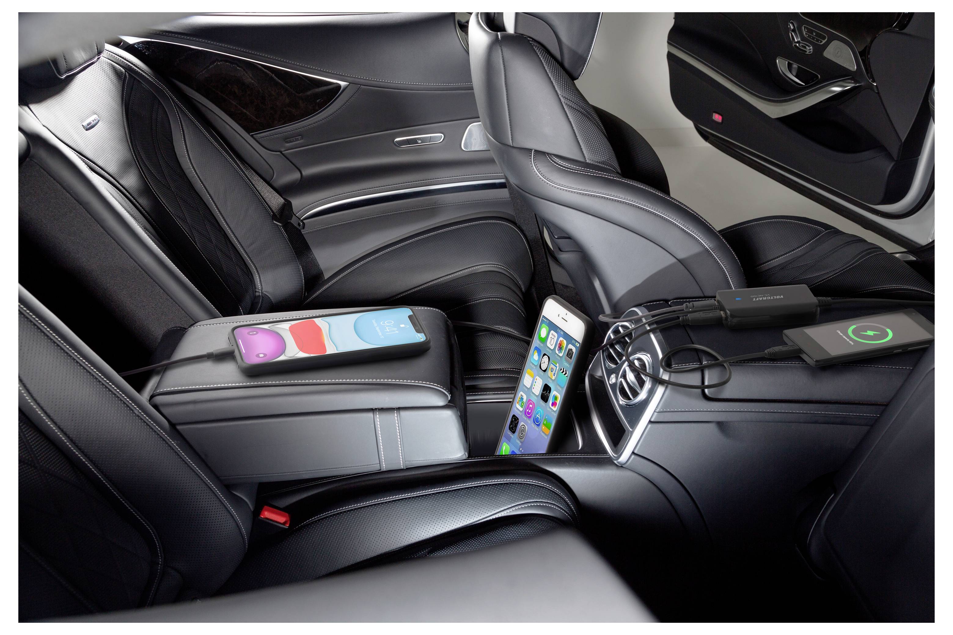Luxusautoinnenraum mit schwarzen Ledersitzen, einem Smartphone in der mittleren Mittelkonsole und Ladekabeln, die mit einem kabellosen Ladegerät und einer Powerbank verbunden sind.