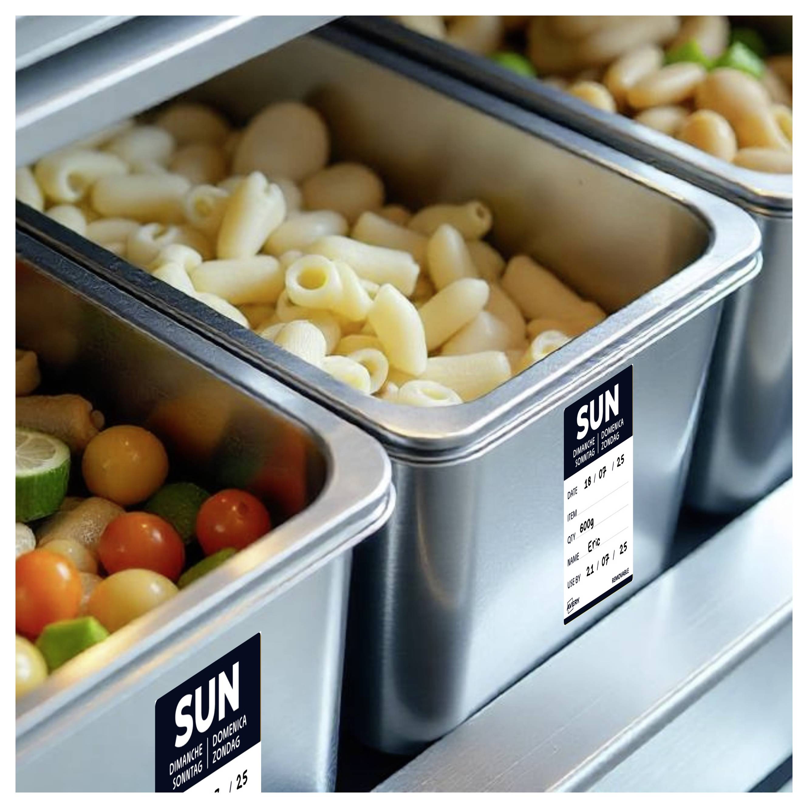 Dampfschalenpfannen gefüllt mit gekochter Pasta und bunten Kirschtomaten in einer Essensausgabe-Buffetlinie mit Preisschildern.