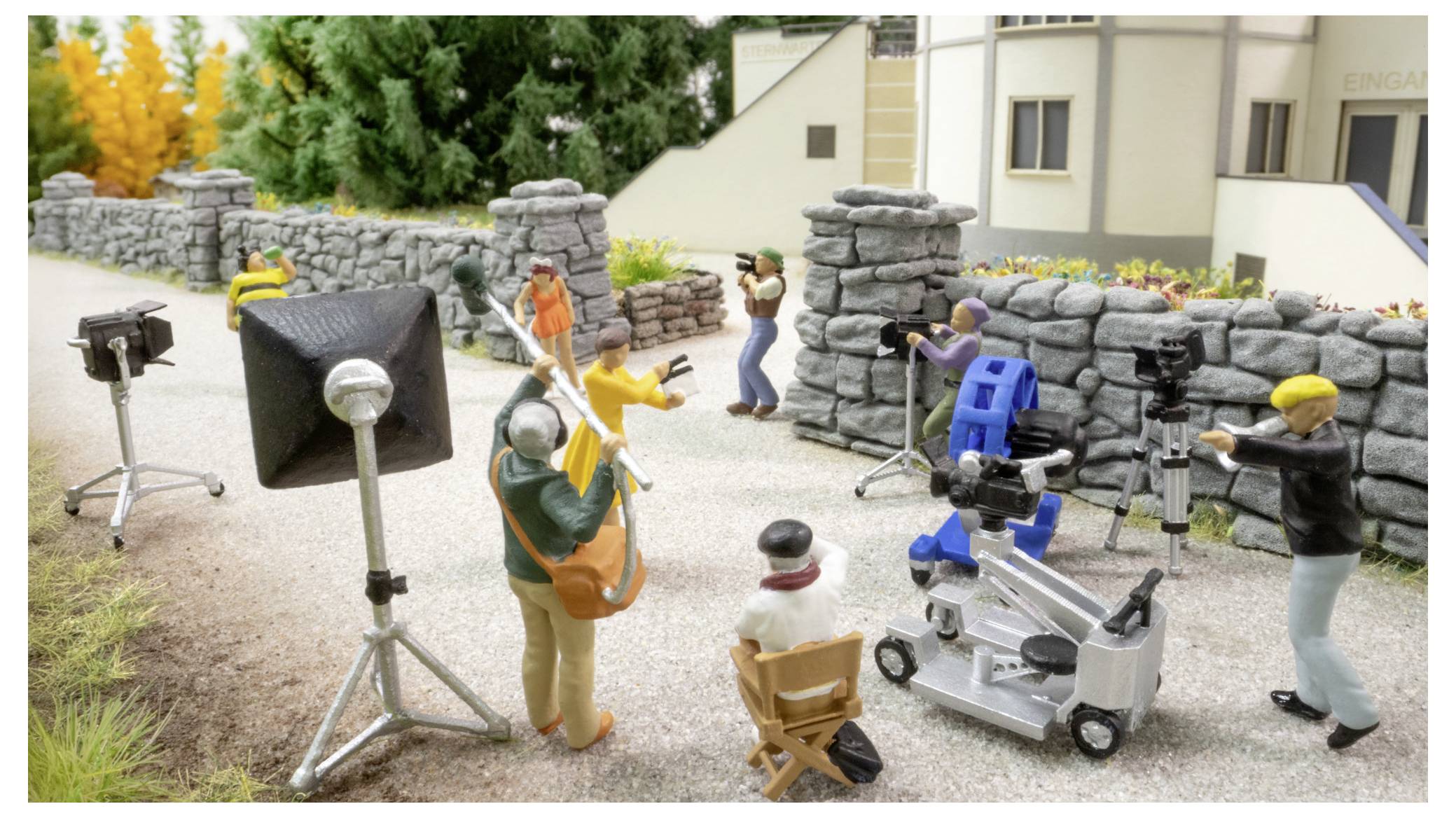 Miniatur-Filmset mit Crew und Kameraausrüstung, das Schauspieler an einer Steinmauer im Freien filmt.