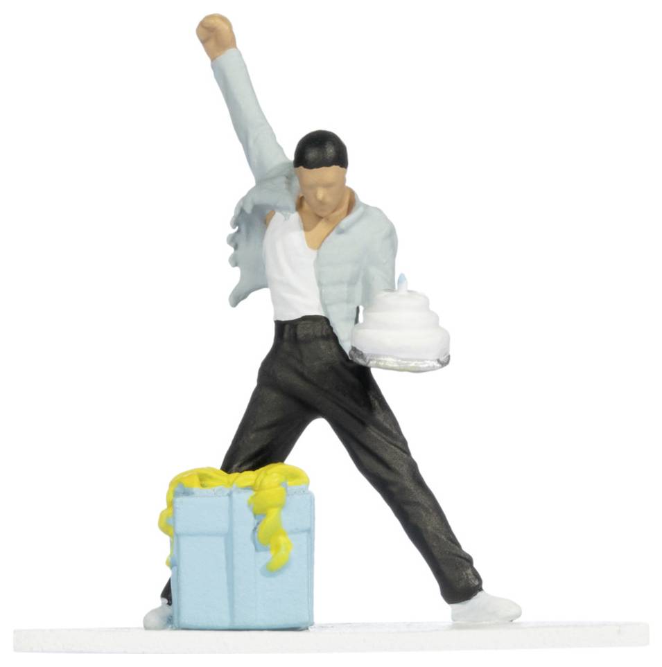 Eine kleine Figur eines Mannes in einer Siegespose neben einer blauen Geschenkbox, der einen gefrorenen Kuchen oder ein Dessert hält.