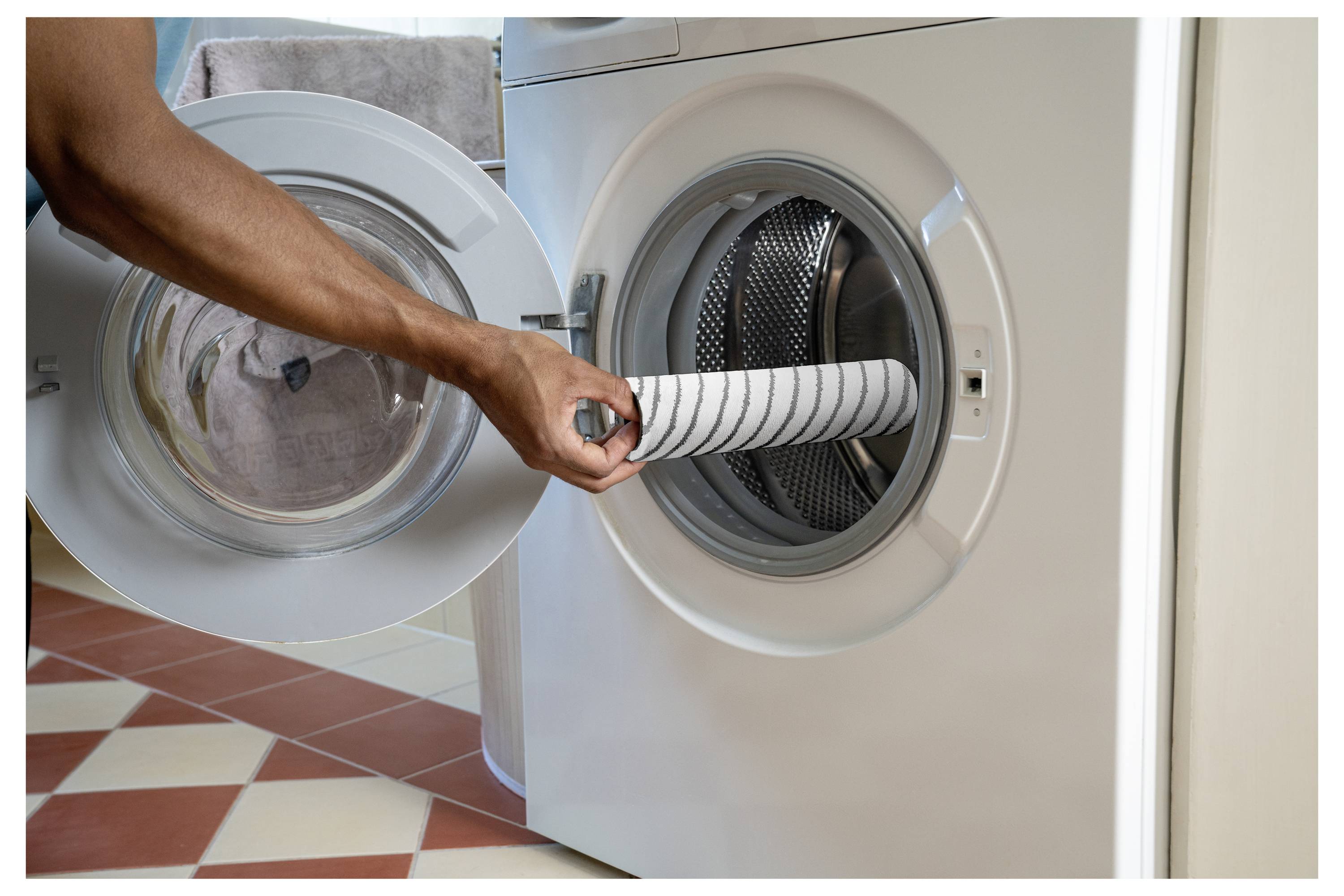 Eine Person lädt ein gestreiftes Handtuch in eine Frontlader-Waschmaschine.