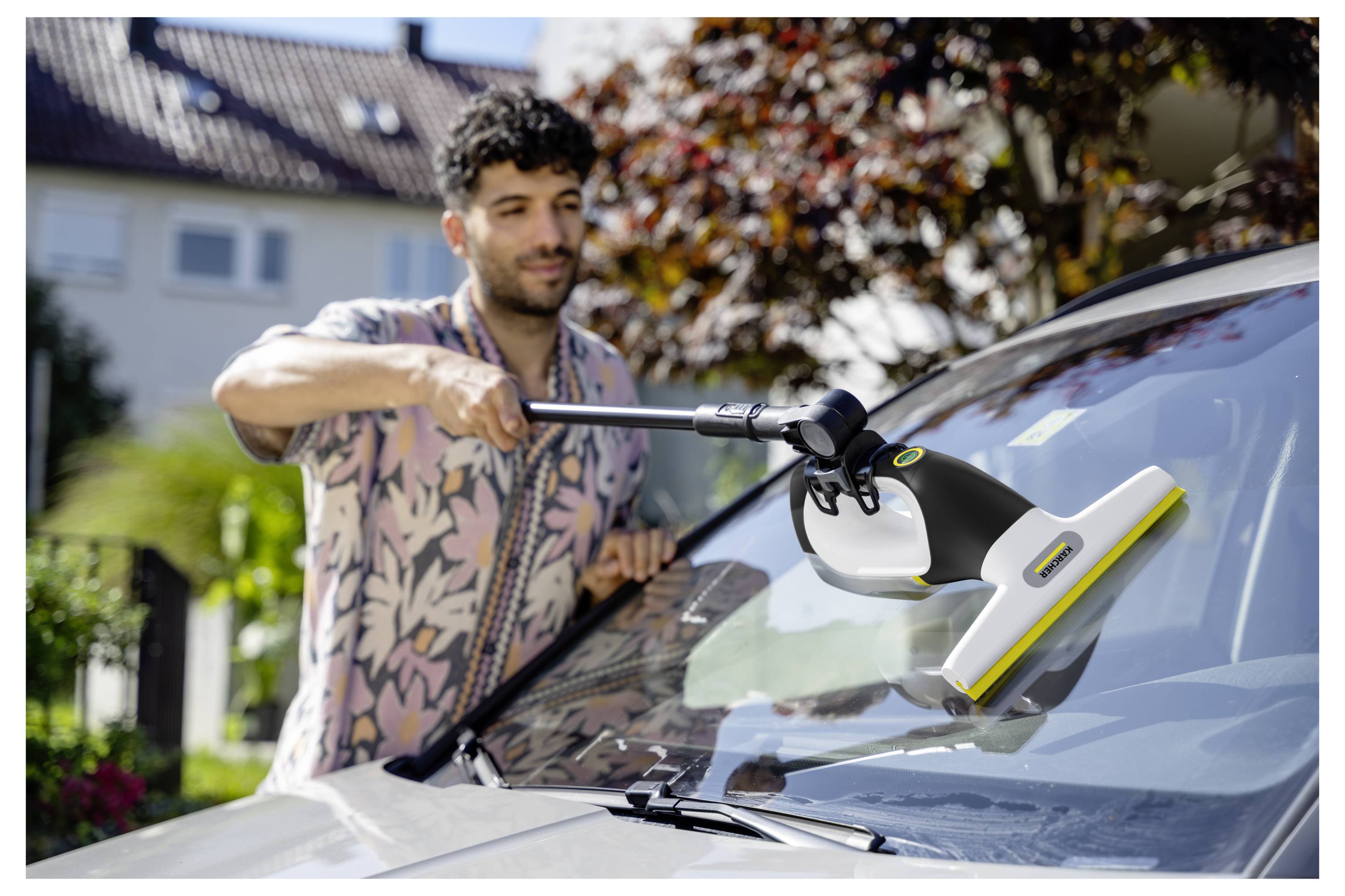 Ein Mann benutzt ein Scheibenwischwerkzeug auf der Windschutzscheibe eines Autos in einer Auffahrt in einem Vorort.