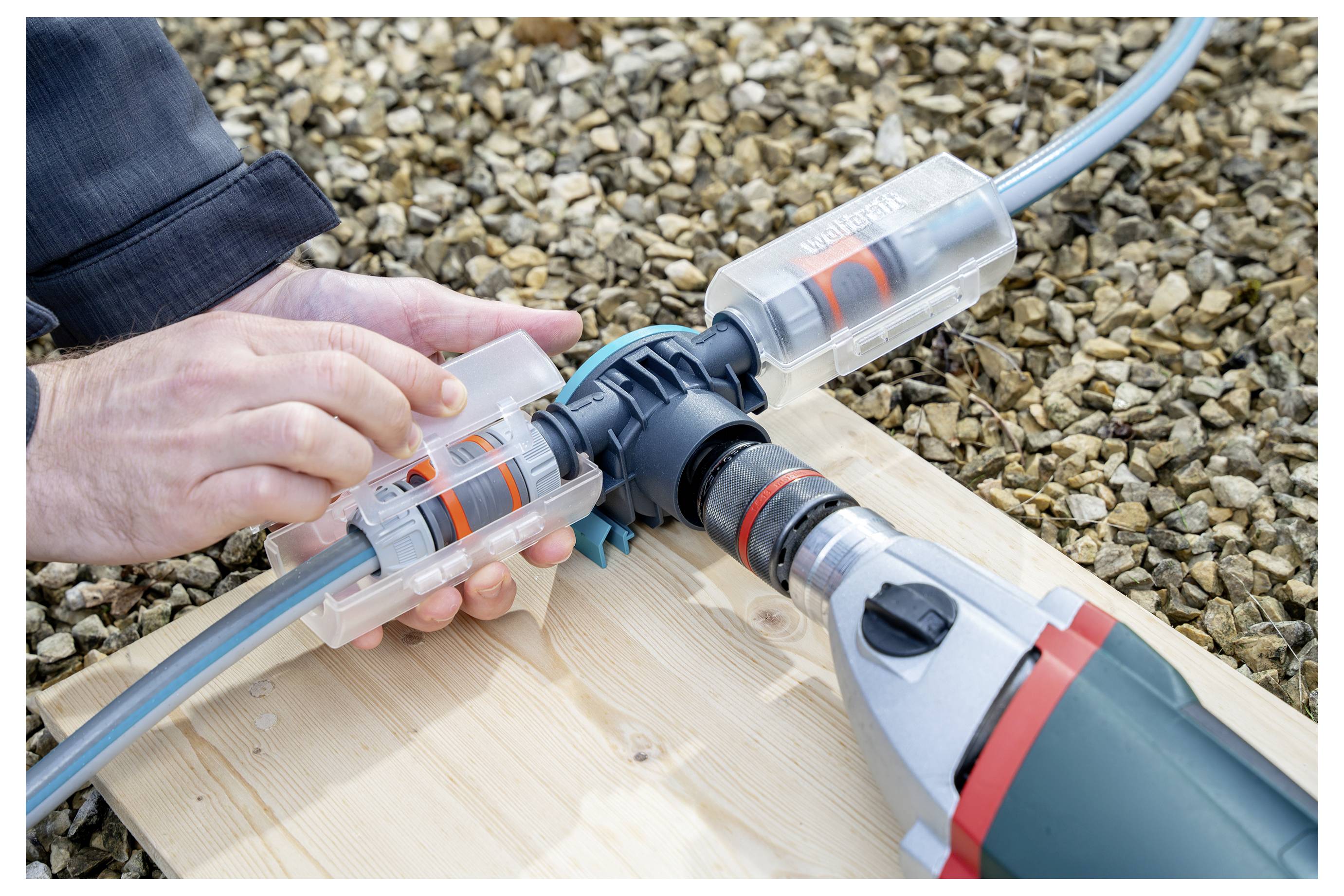 Hand, die einen Gartenschlauch mit einem Kunststoff-Schnellverbinder auf einer Holzplatte im Freien anschließt.