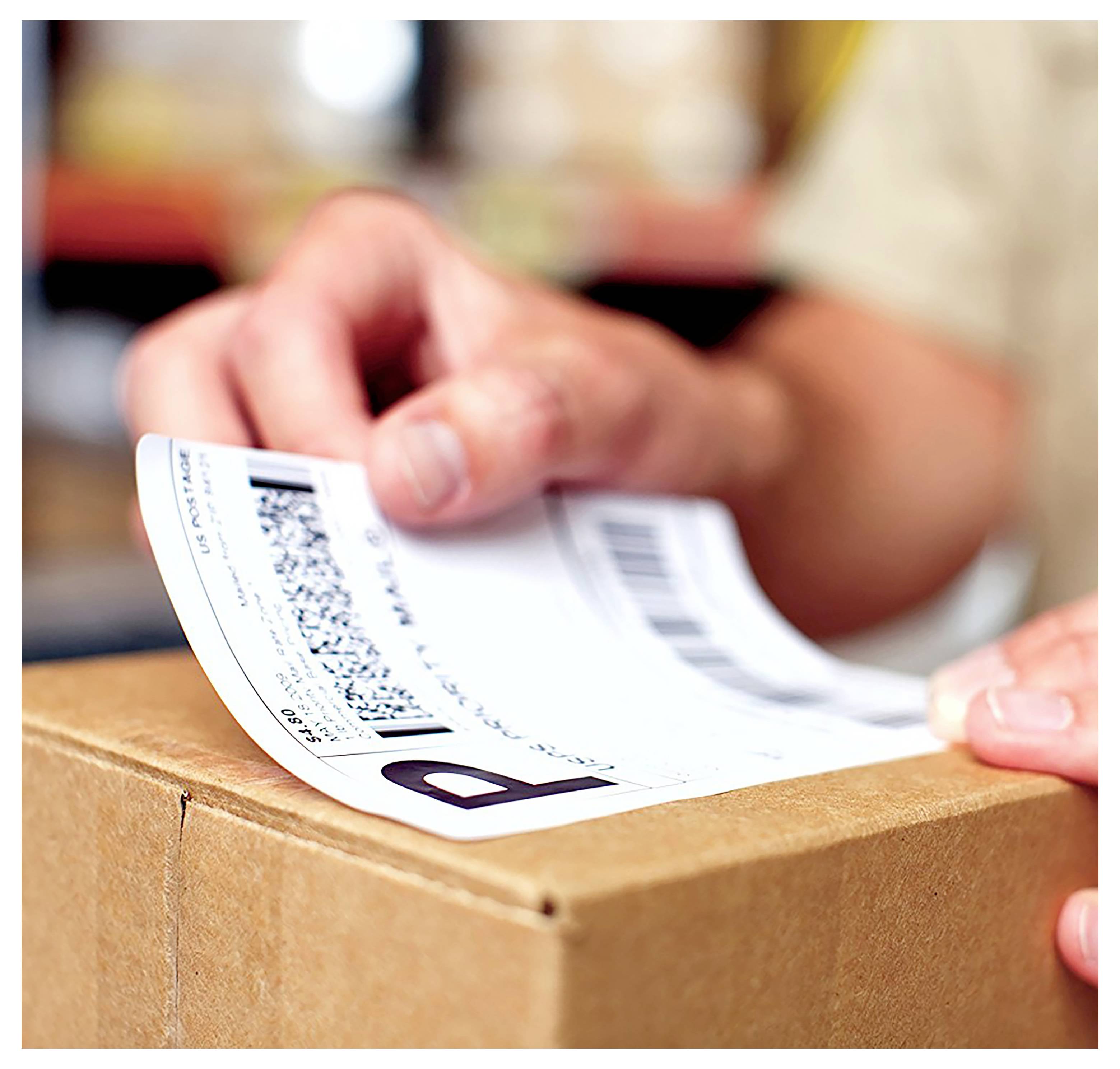 Eine Person bringt ein Versandetikett auf einem Kartonkarton an und bereitet ein Paket zum Versand oder zur Zustellung vor.