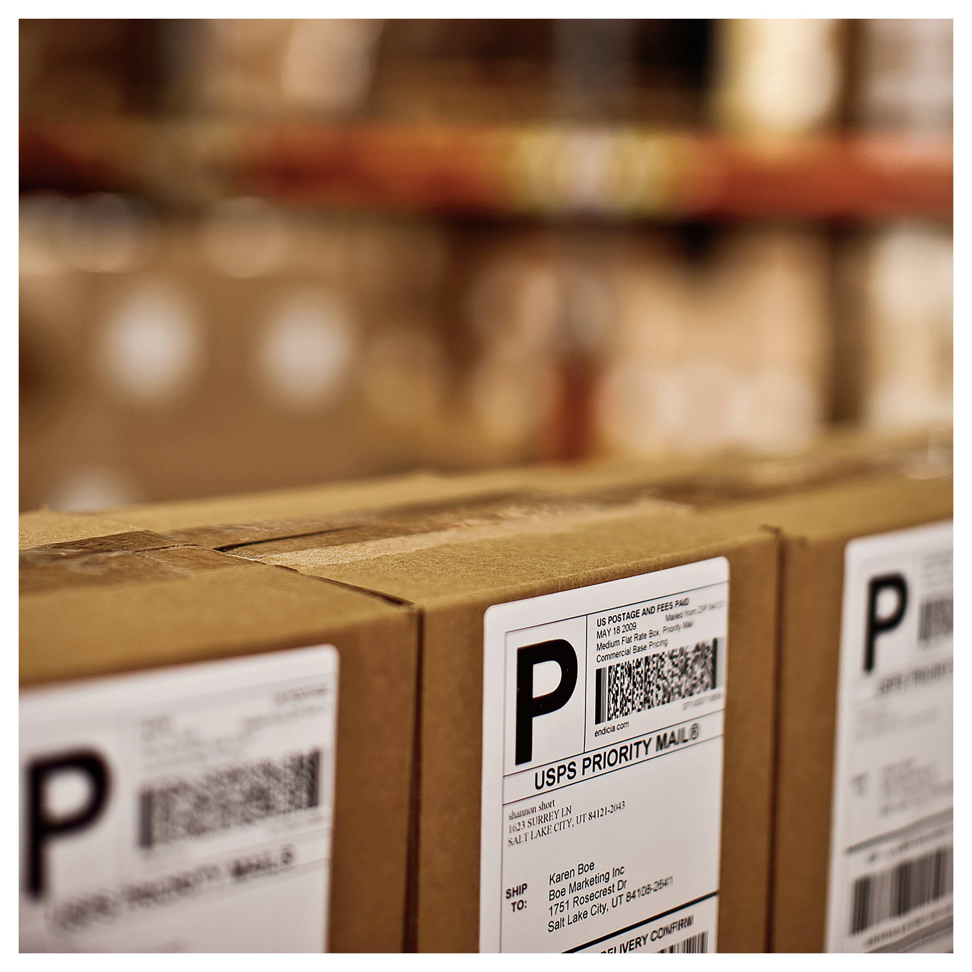 Nahaufnahme von USPS-Prioritätspostboxen mit Versandetiketten und Strichcodes in einem Lager- oder Postbearbeitungsbereich.