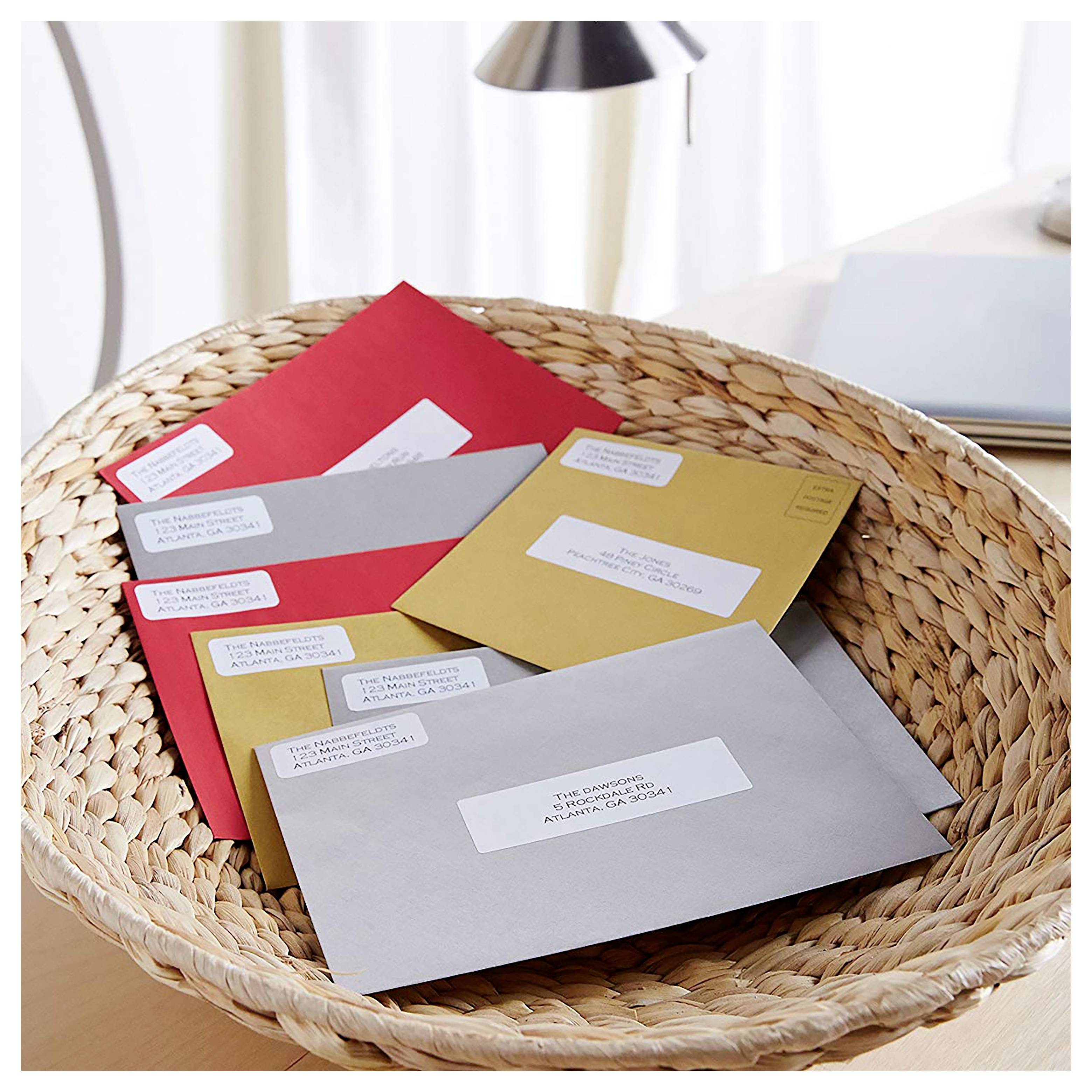 Geflochtener Korb mit mehreren adressierten Umschlägen in Rot, Grau, Gold und Weiß auf einem Schreibtisch.