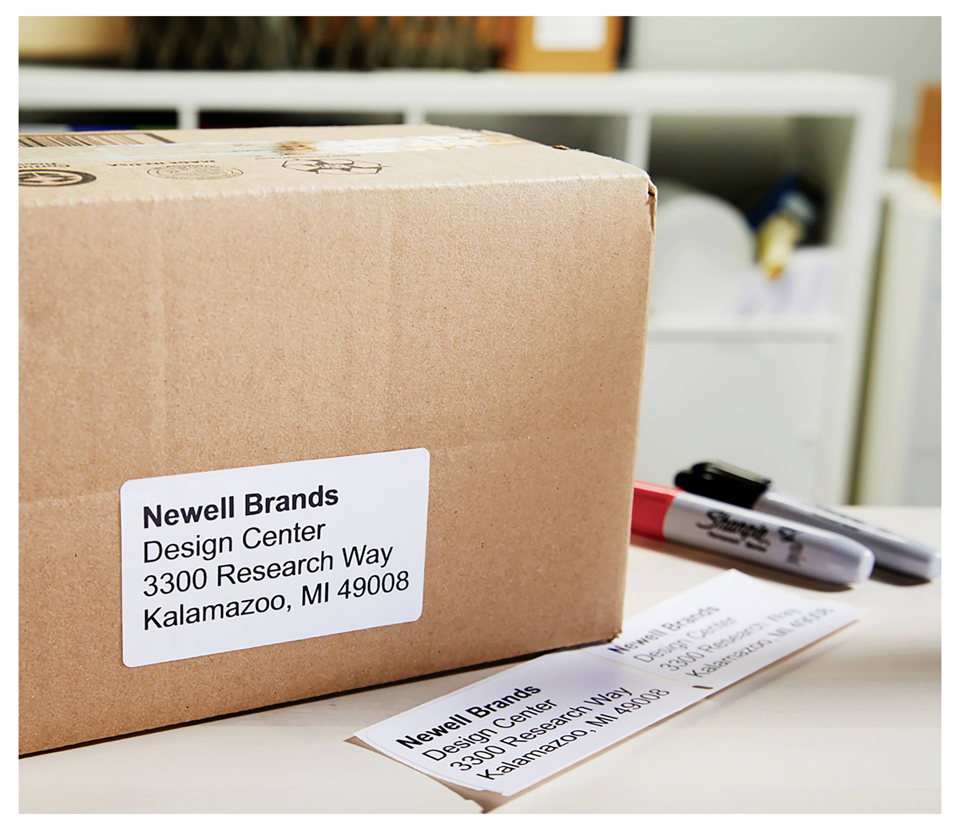 Ein Versandkarton mit einem Adressenetikett der Marke Newell Brands liegt auf einem Schreibtisch neben einem Marker und einem zweiten Versandetikett.
