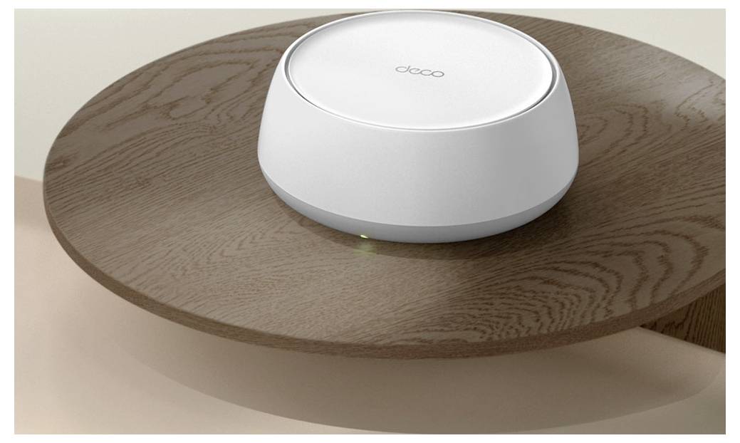 Ein weißer Deco Wi-Fi Router sitzt auf einem runden Holztisch und zeigt ein kleines grünes Statuslicht.