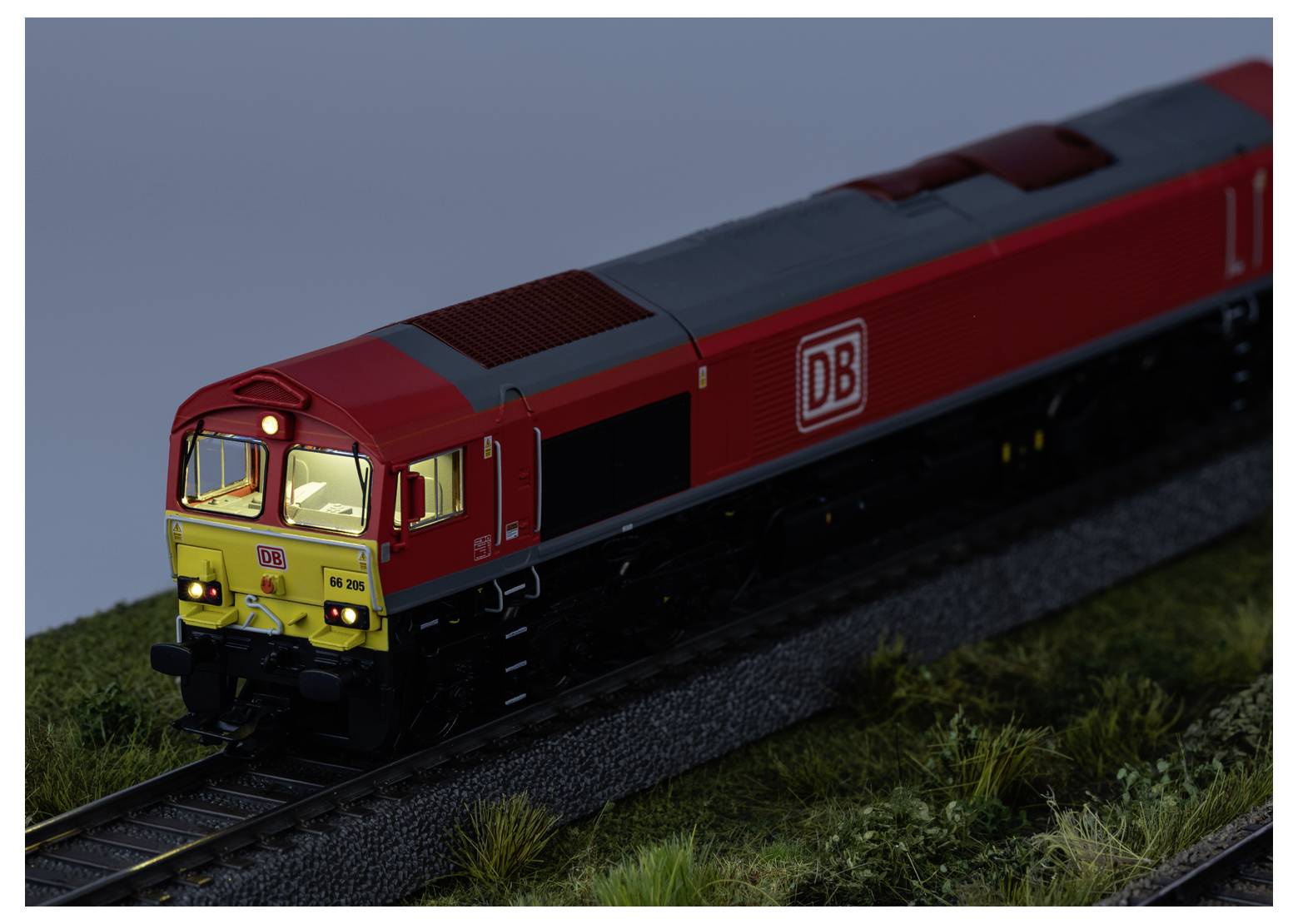 Rote DB-Güterzuglomotive auf Modelleisenbahngleisen, von vorne-links in der Dämmerung betrachtet.