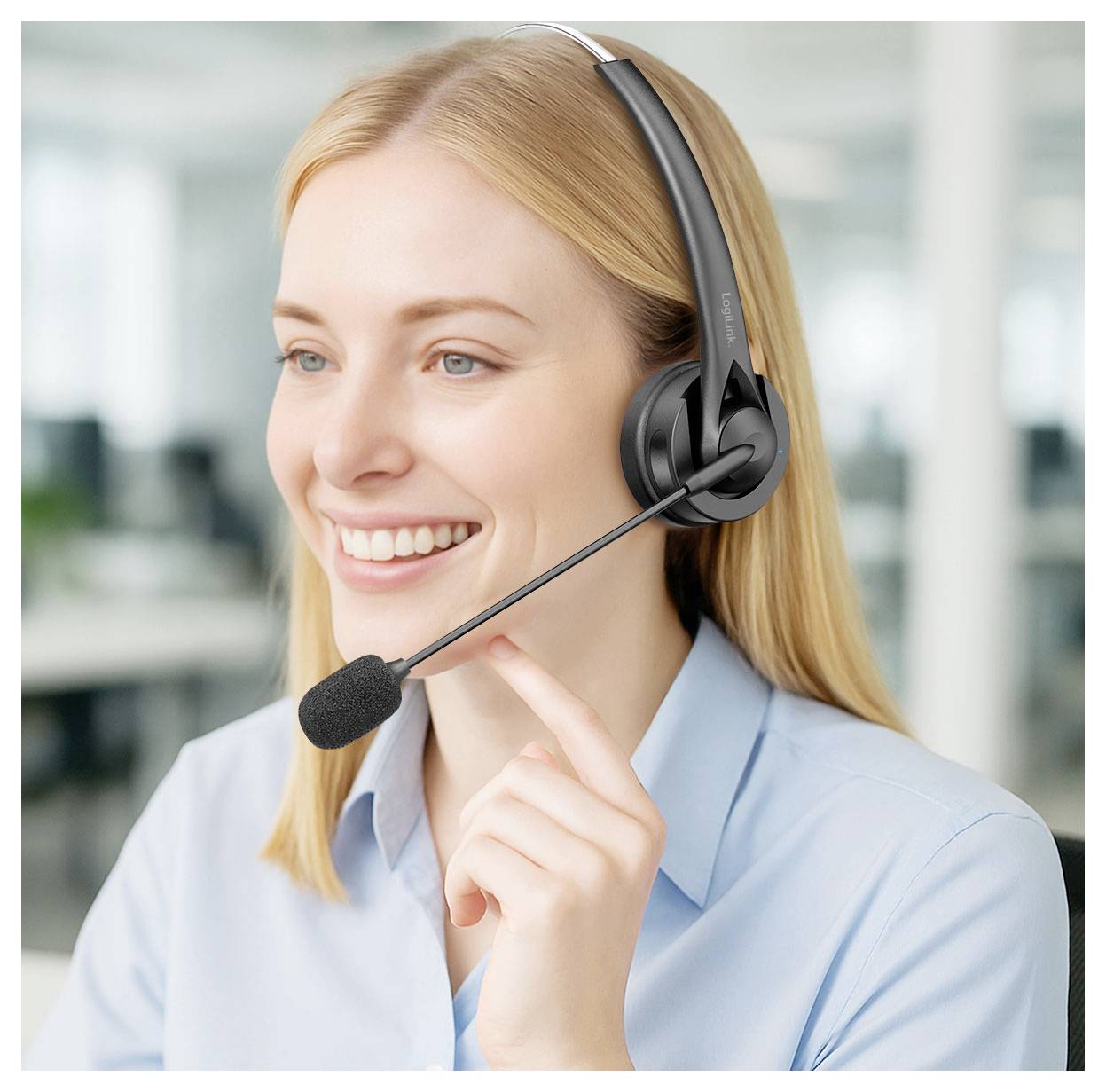 Lächelnde Frau, die ein Headset-Mikrofon trägt, was auf eine Kundenservice- oder Call-Center-Mitarbeiterin in einer Büroumgebung hindeutet.