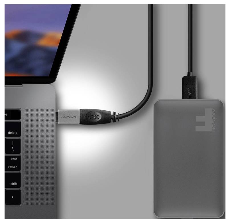 Laptop, das über ein Kabel mit einem grauen AXAGON-Externe Festplatte oder Hub daneben auf einem Schreibtisch verbunden ist.