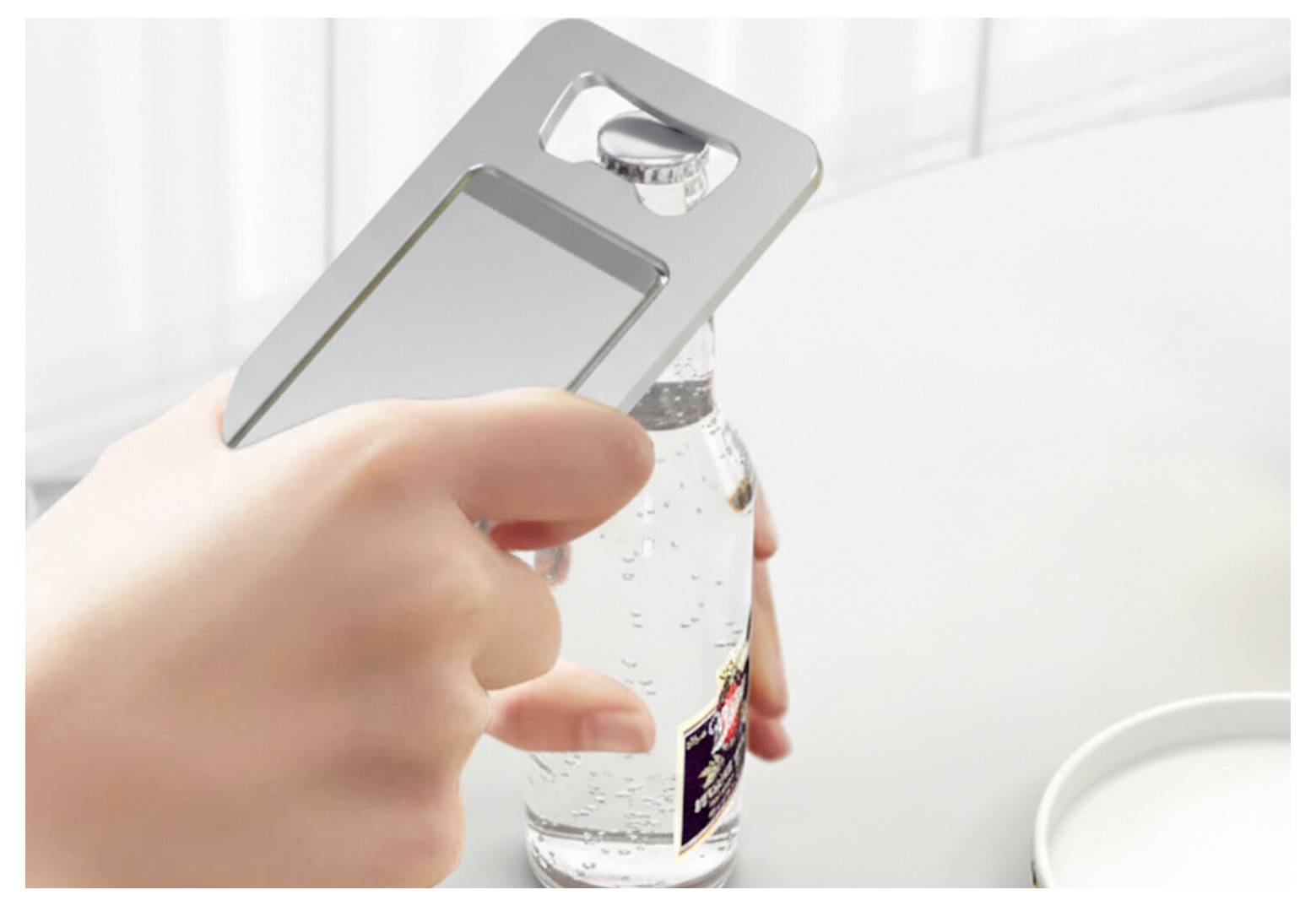Hand, die einen Flaschenöffner verwendet, um die Kappe von einer Glasflasche auf einer weißen Oberfläche abzuhebeln.