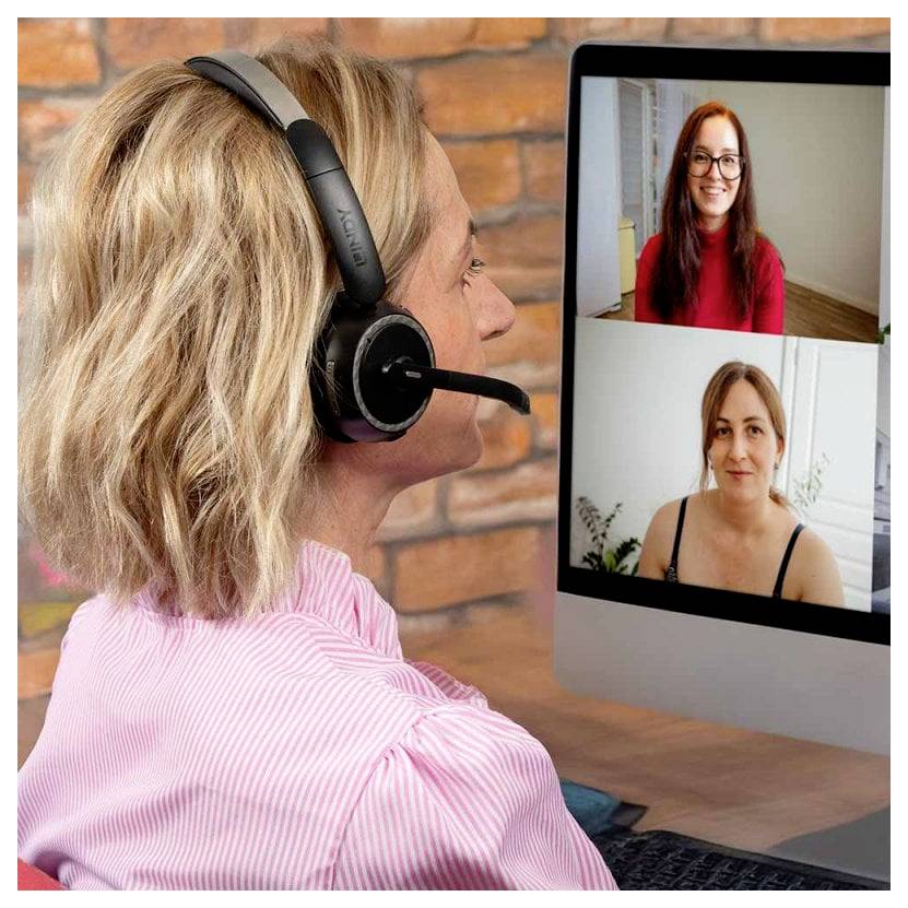 Frau mit Headset spricht in einem Videoanruf mit zwei Frauen, die auf einem Desktopmonitor im Split-Screen angezeigt werden.