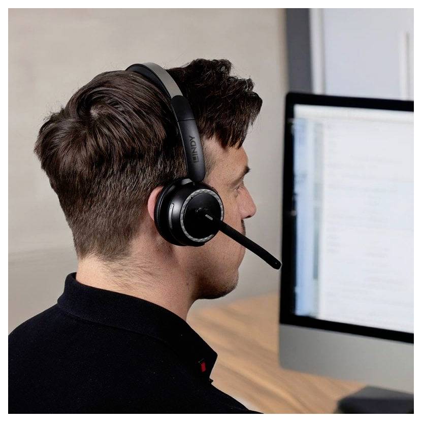 Ein Mann mit Kopfhörer arbeitet an einem Desktop-Computer, von hinten und im Profil betrachtet.