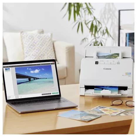Laptop, der mit einem Canon-Fotodrucker verbunden ist, druckt farbenfrohe Fotos auf einem Tisch, mit ausgedruckten Bildern und Gläsern in der Nähe in einer häuslichen Umgebung.