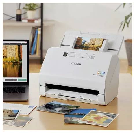 Canon-Fotodrucker druckt Bilder von einem Laptop, mit mehreren gedruckten Fotos, die auf einem Schreibtisch verteilt sind.