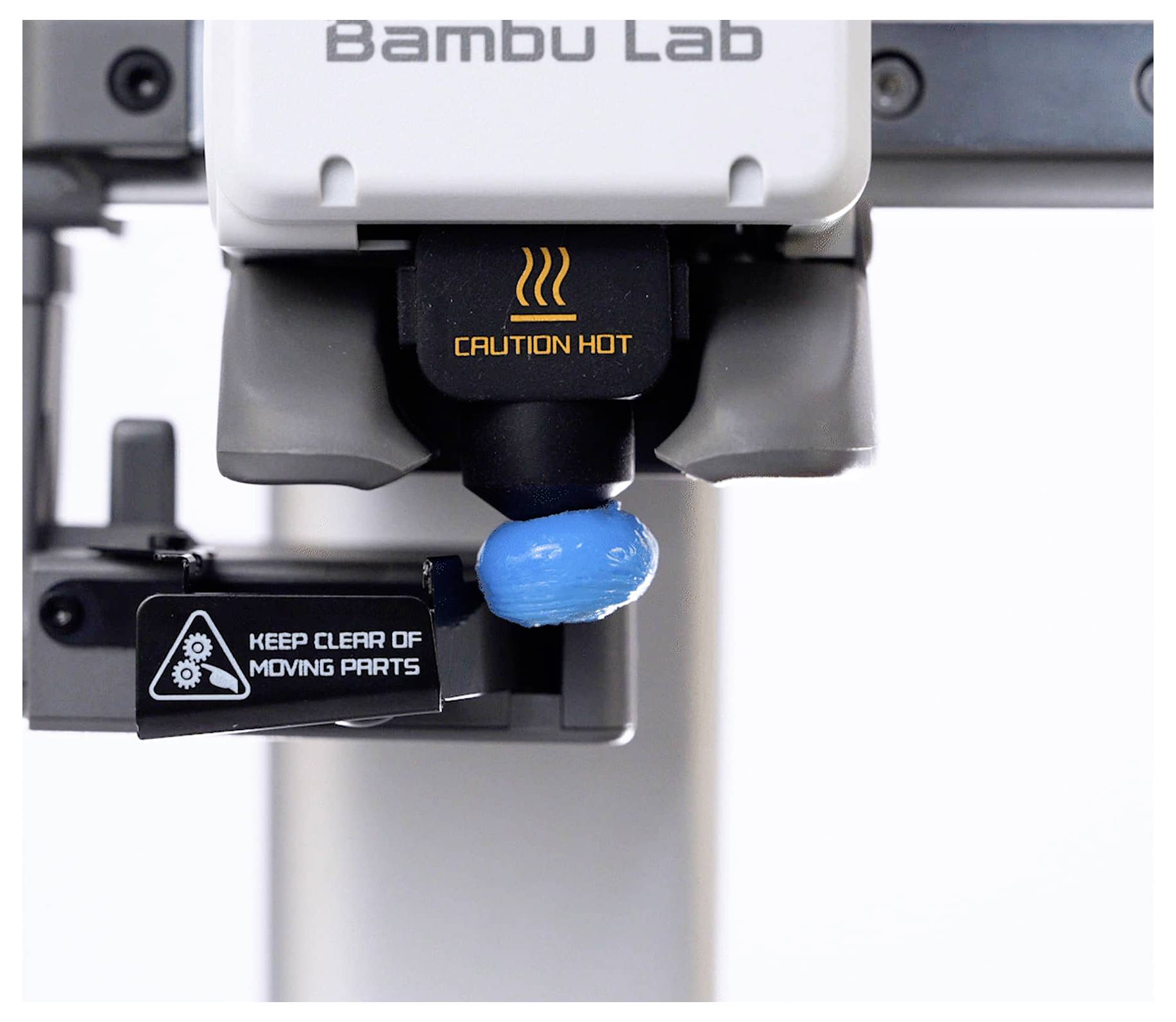Nahaufnahme eines Bambu Lab 3D-Druckers-Extruders beim Drucken eines blauen Objekts, wobei die Warnhinweise „CAUTION HOT