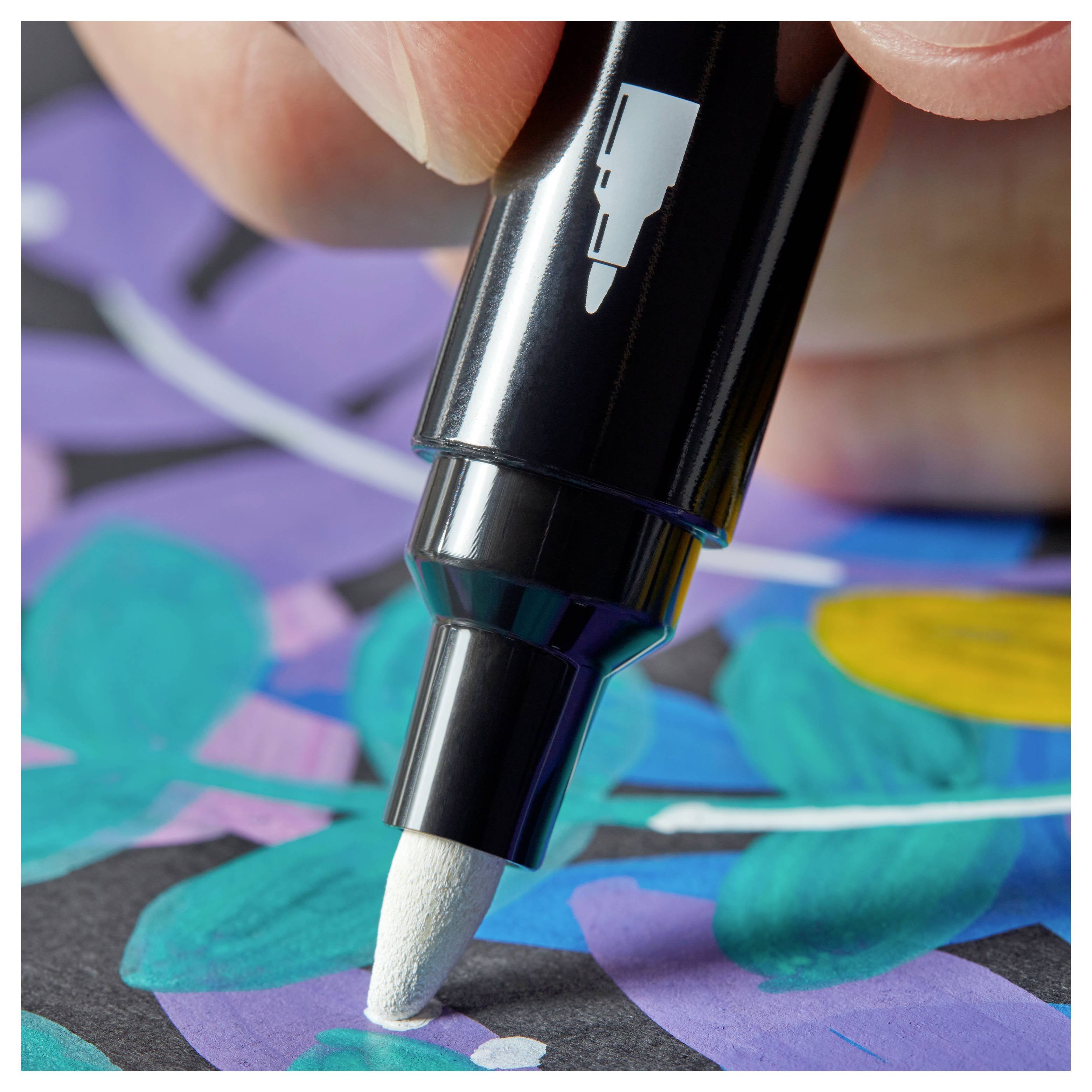 Nahaufnahme einer Hand, die mit einem weißen Malstift weiße Details auf einem bunten abstrakten Kunstwerk hinzufügt.