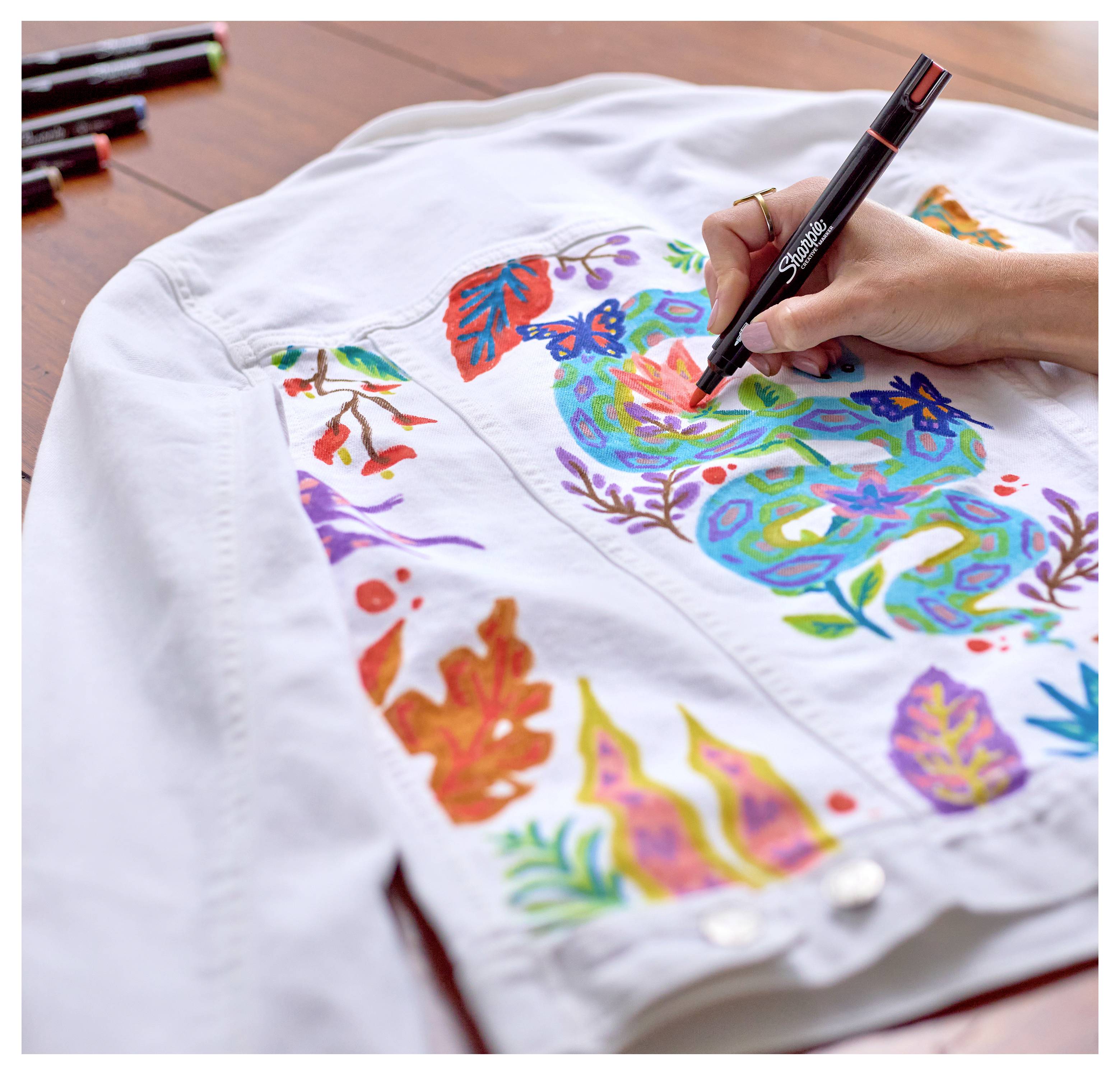 Mit einem schwarzen Marker bunte Blumen- und Blattmuster von Hand auf eine weiße Jacke zeichnen.
