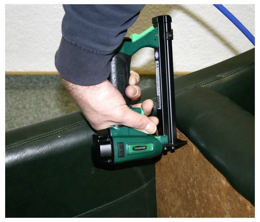 Hand, die einen grünen Polsternagelhefter verwendet, um Material an einem Stuhlrahmen oder Kissen zu befestigen