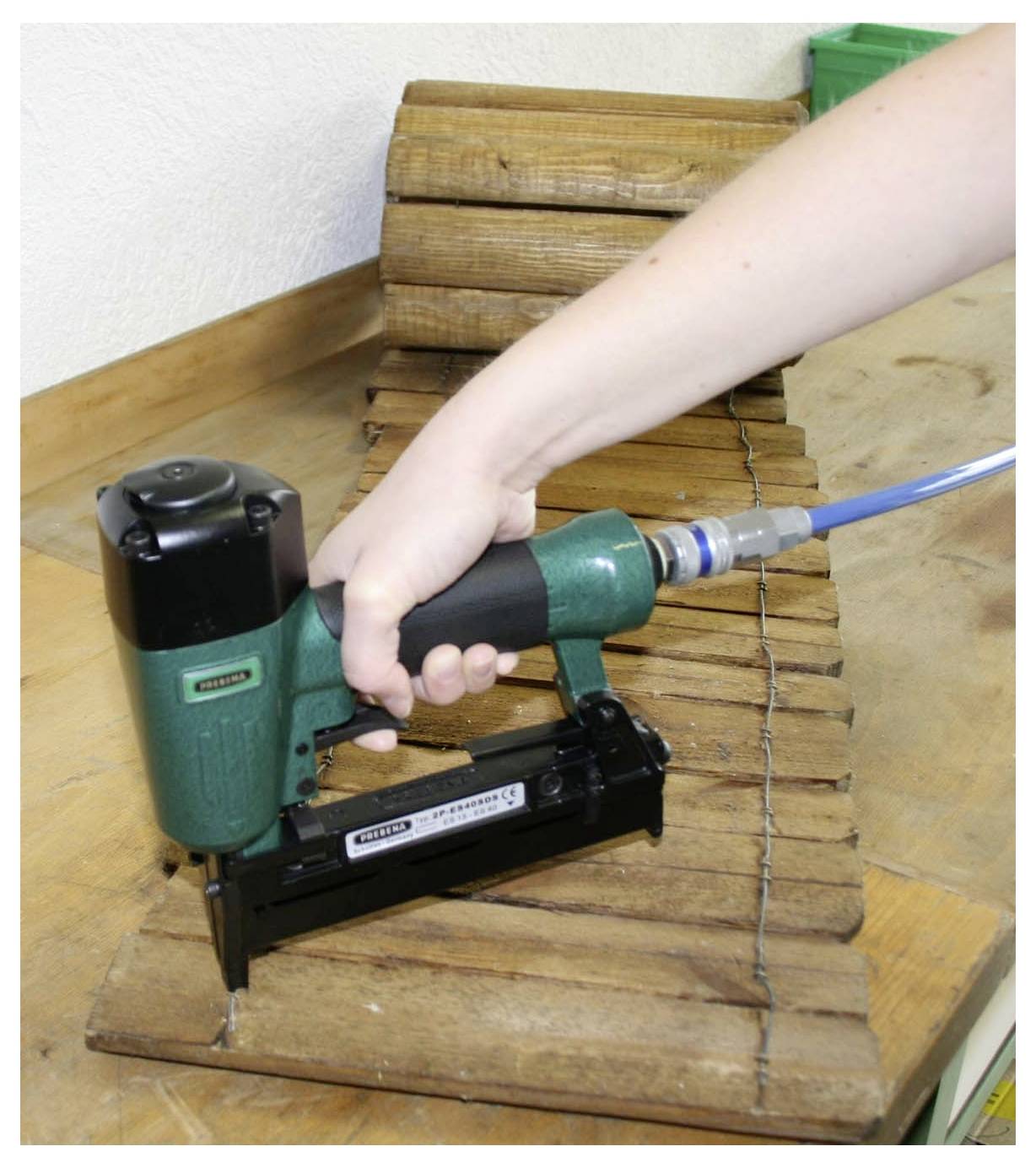 Person, die ein pneumatisches Nagelpistole benutzt, um Holzleisten auf einer gekrümmten Holzoberfläche zu befestigen.