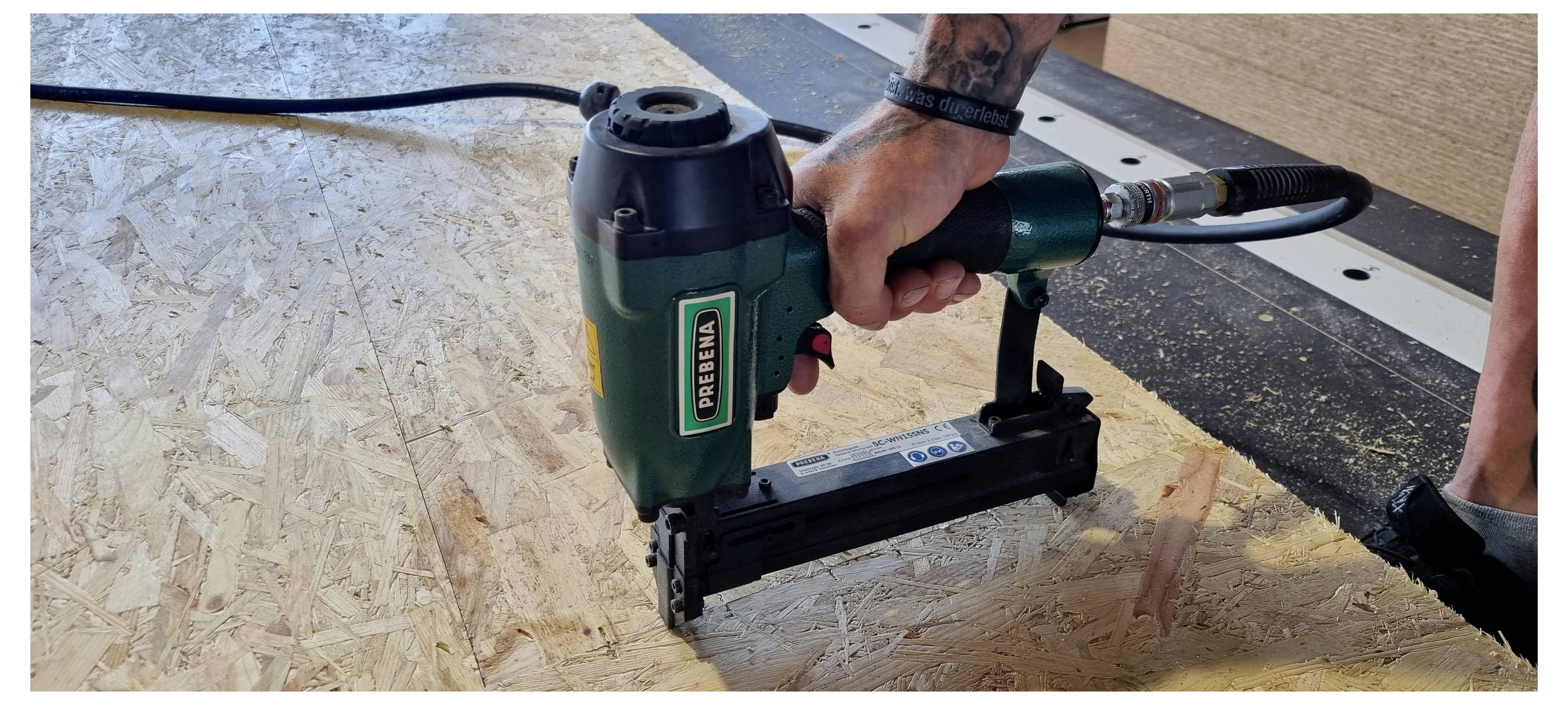 Person verwendet eine grüne DeWalt-Nagelmaschine, um Sperrholz auf einem Boden oder einer Arbeitsfläche zu befestigen.