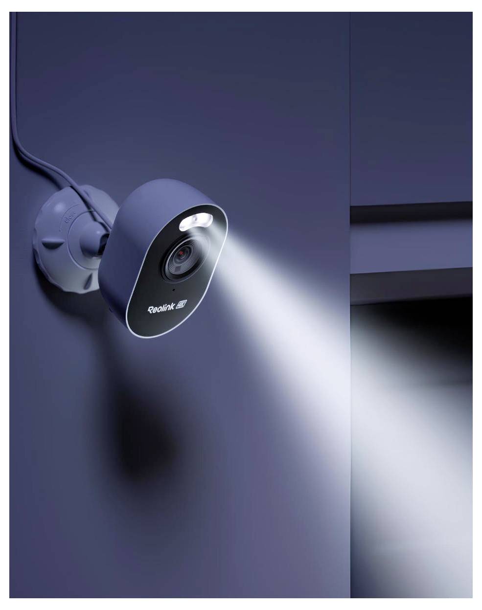 An der Wand montierte Sicherheitskamera an einer dunklen Außenwand, die einen hellen Lichtstrahl nach rechts projiziert.