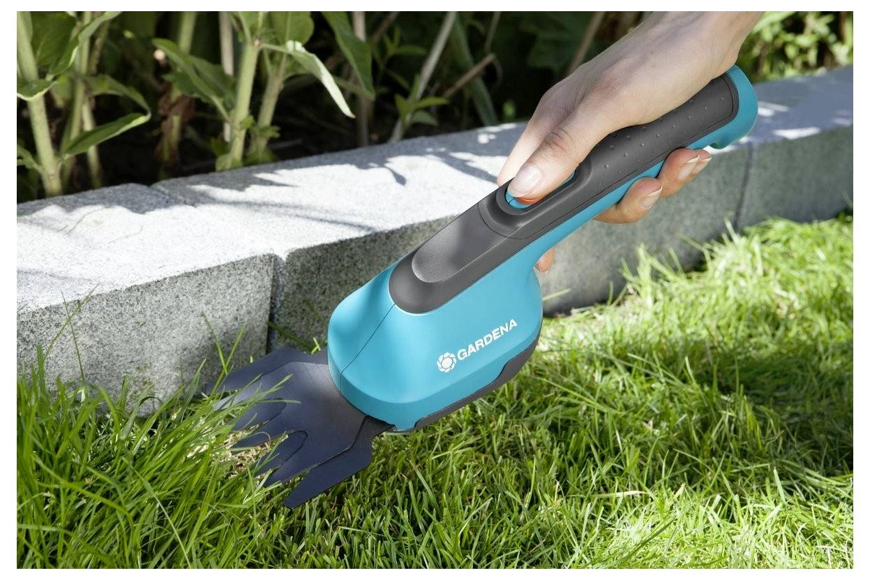 Eine Hand benutzt einen kabellosen GARDENA Rasentrimmer, um Gras entlang einer Steinkante zu schneiden.