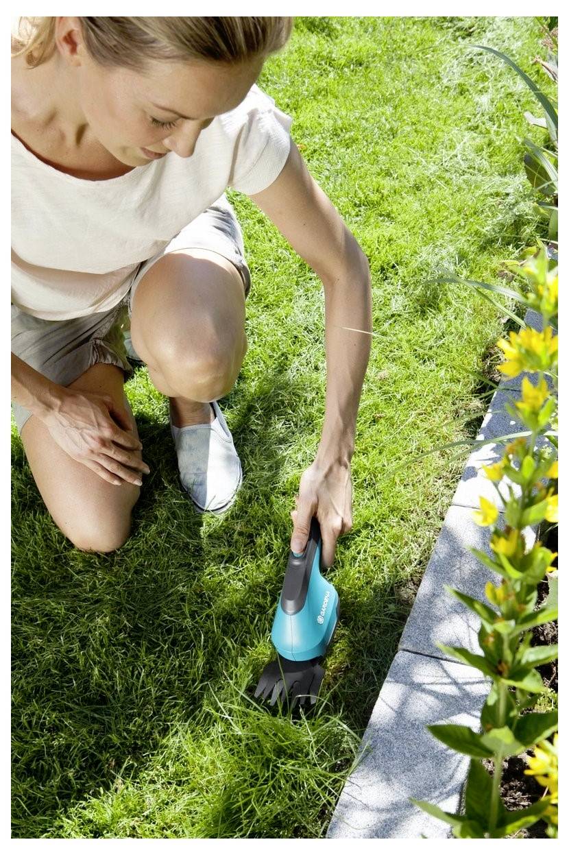 Frau kniet auf dem Gras und verwendet einen kleinen blauen elektrischen Trimmer, um den Rasen neben einem Blumenbeet zu kanten.