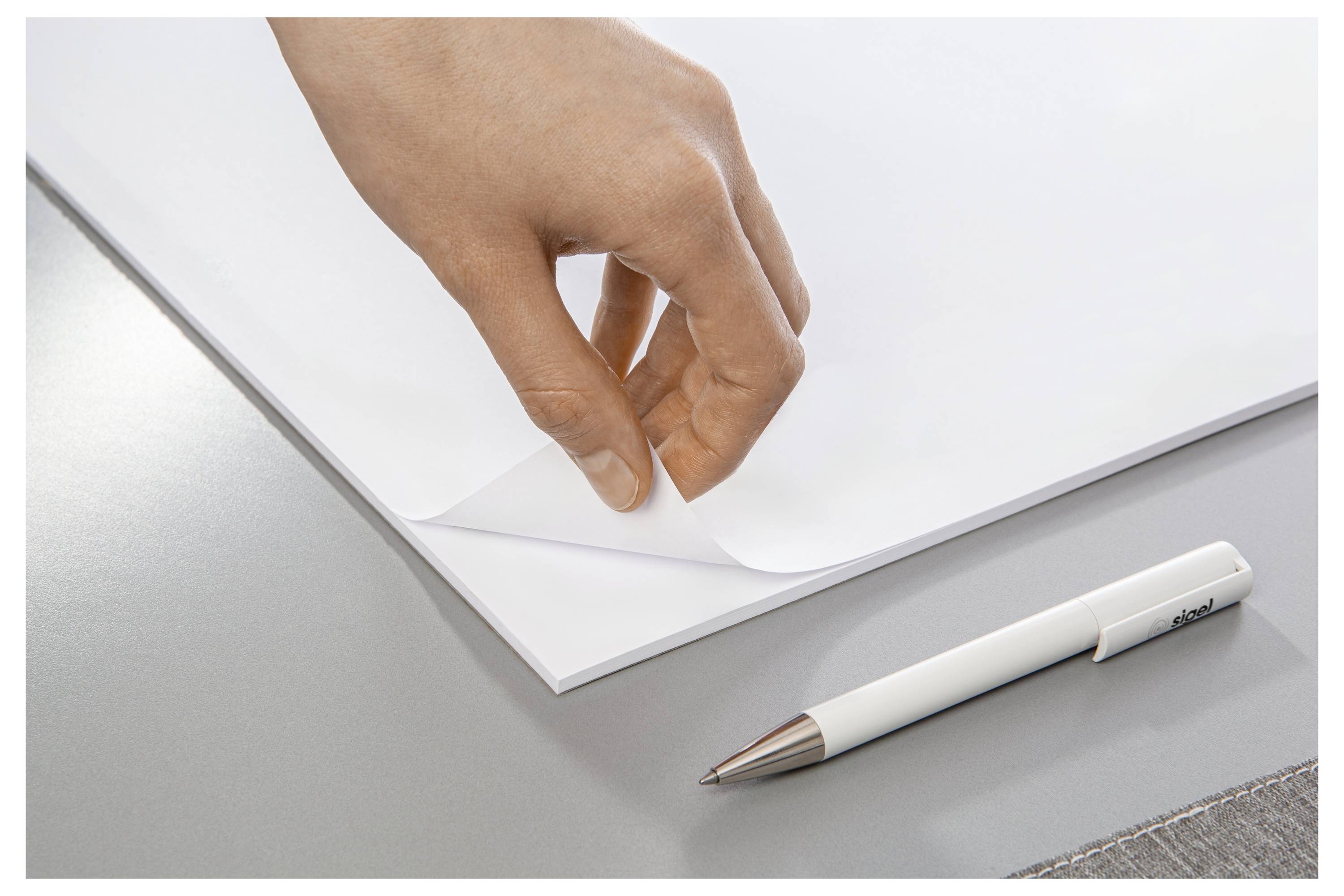 Eine Hand, die eine Ecke eines leeren weißen Blattes Papier neben einem weißen Stift auf einem grauen Schreibtisch zurückzieht.