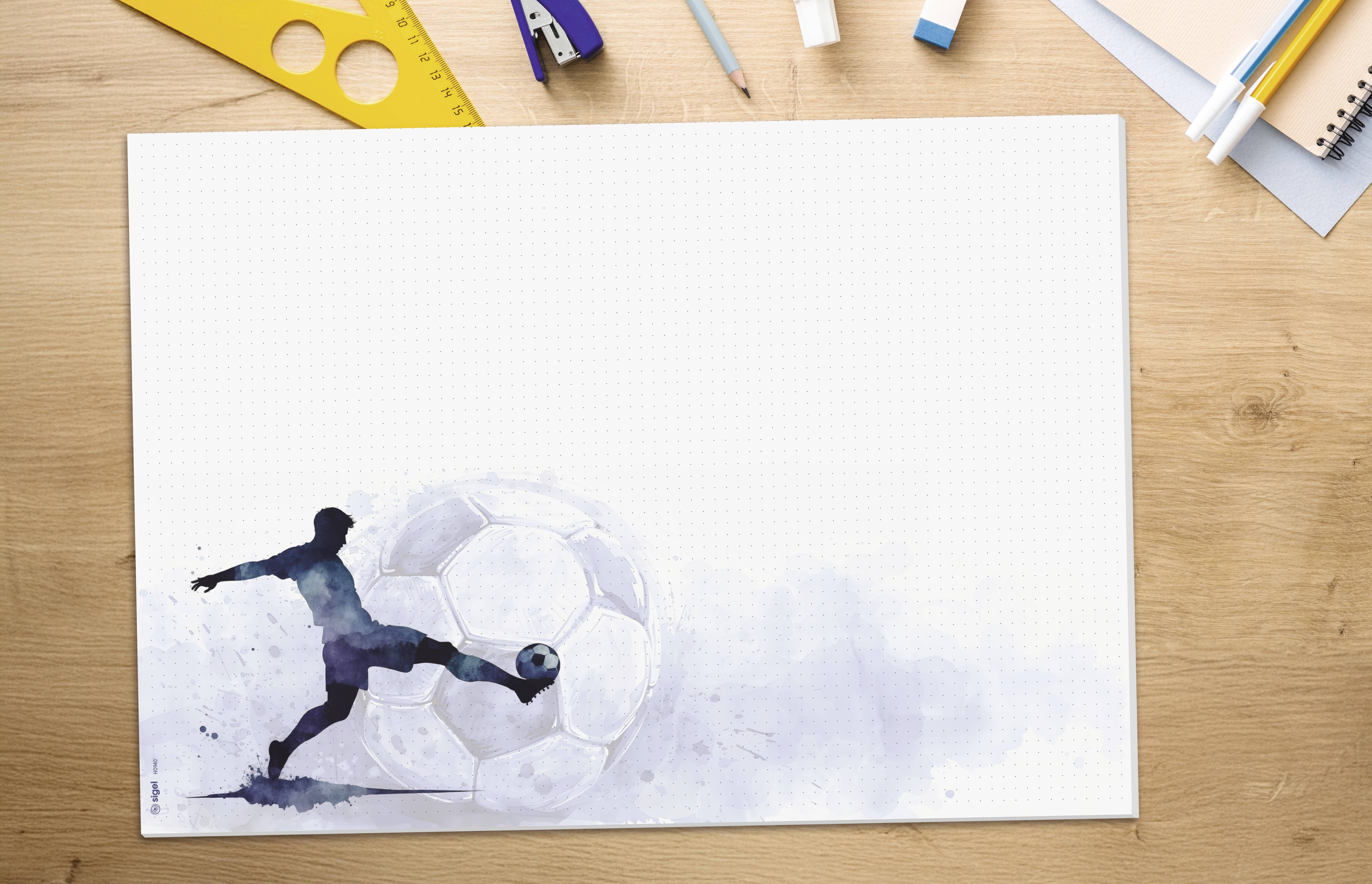 Aquarell-ähnliche Illustration eines Fußballspielers, der einen Ball auf einem größtenteils leeren Blatt Papier tritt, betrachtet auf einem Schreibtisch mit Art-Supplies rundherum.