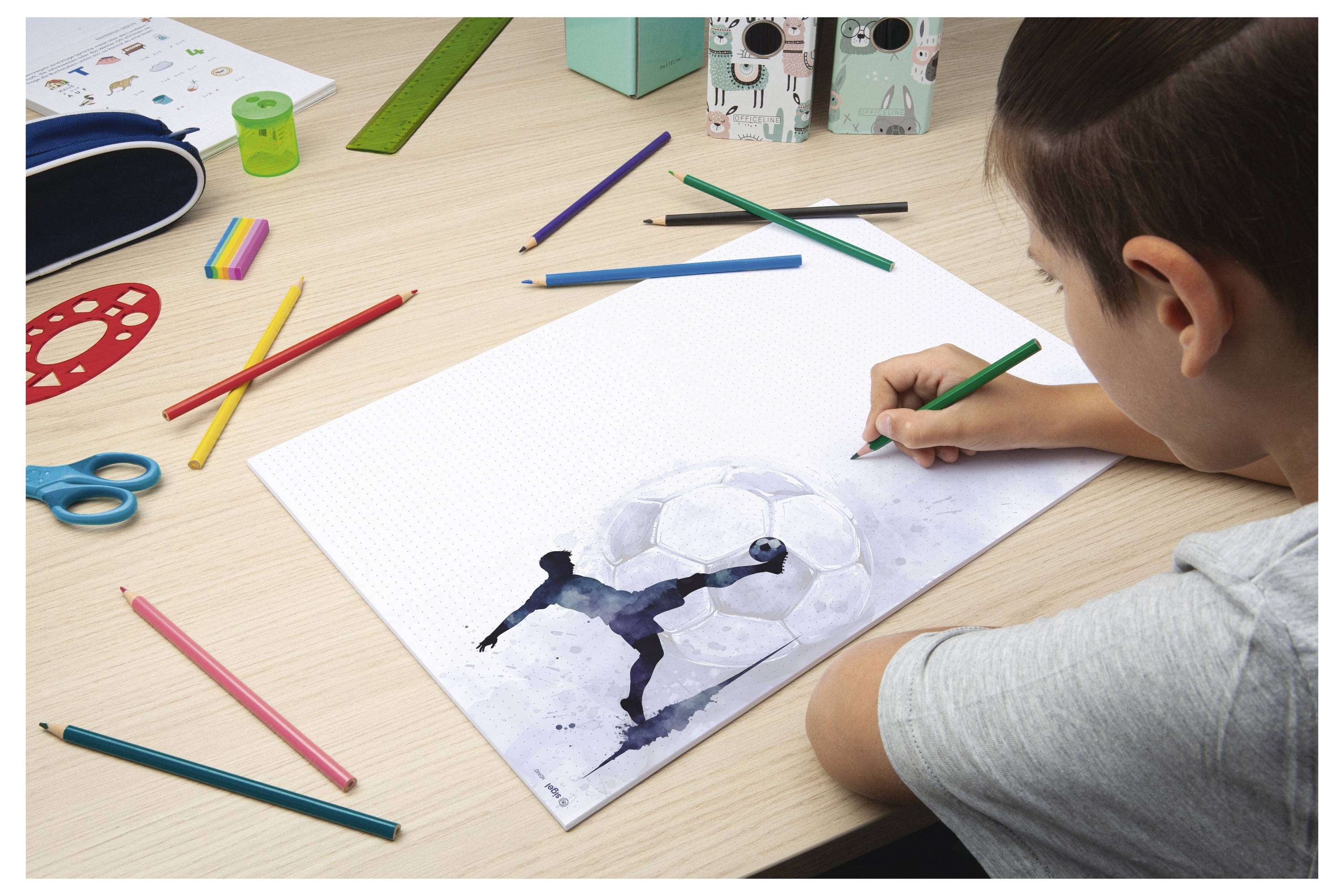 Ein Kind zeichnet einen Fußballspieler auf einem Blatt Papier an einem Schreibtisch mit Buntstiften und Scheren, die herum verstreut sind.