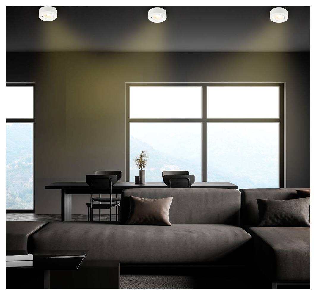 Modernes Wohnzimmer mit dunklem Ecksofa, das auf einen Esstisch ausgerichtet ist, und großen Fenstern mit hellem Außenlicht.