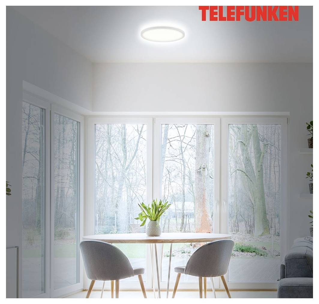 Helle minimalistische Essecke mit rundem Tisch, zwei grauen Stühlen, großen Fenstern mit Waldblick und einer Deckenleuchte mit der Beschriftung „TELEFUNKEN